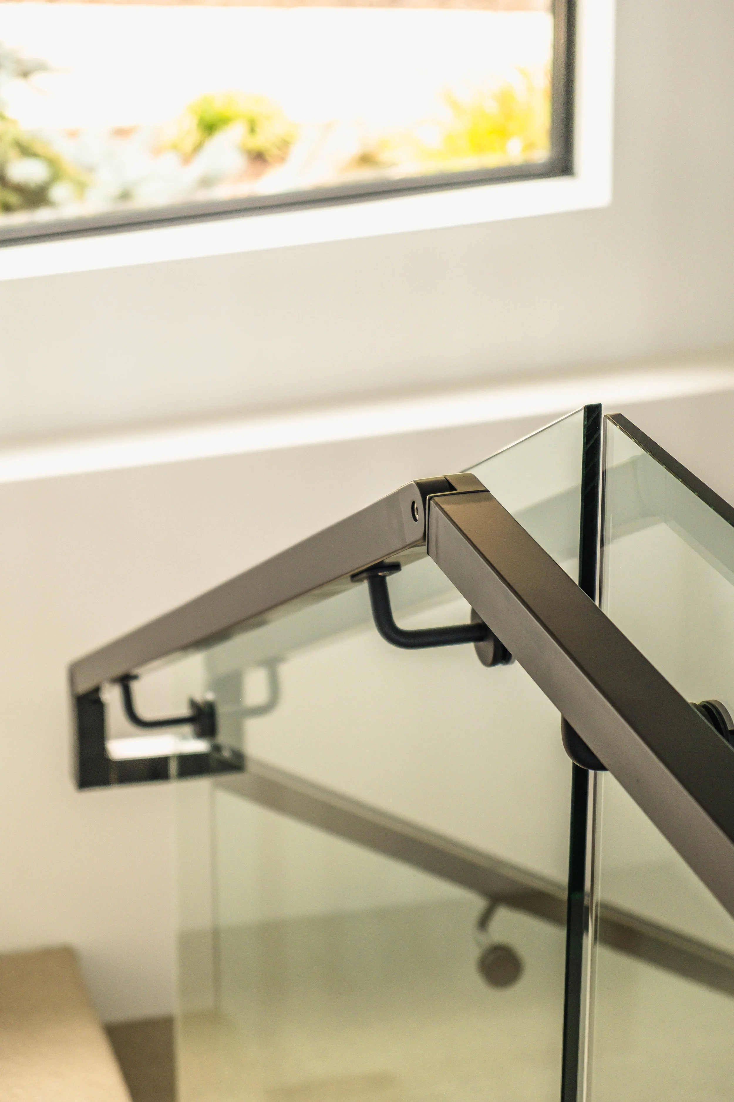 Close-up of a modern glass staircase railing near a window with sunlight coming through.
