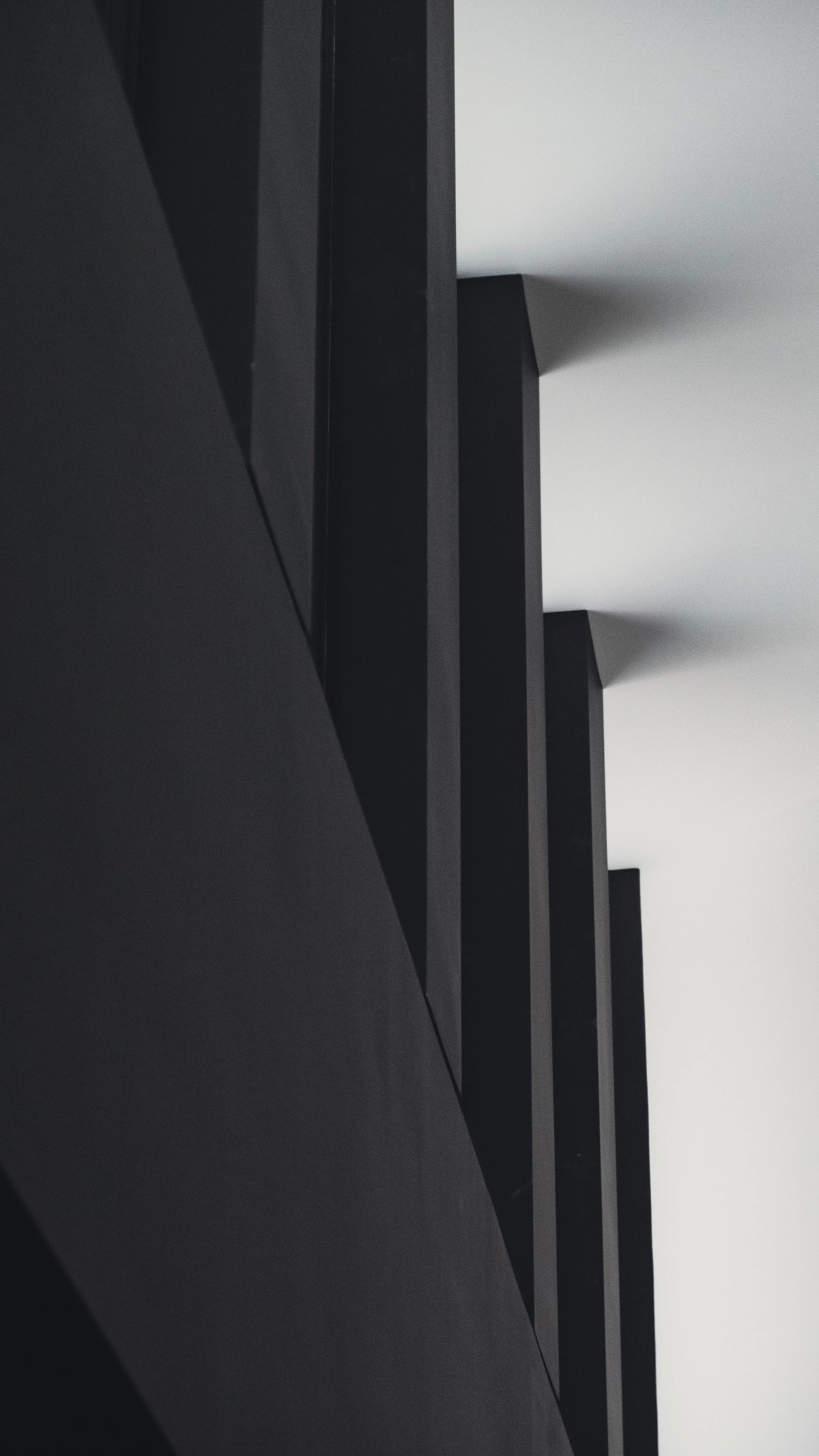Close-up of a modern black staircase with shadows cast on a white wall, emphasizing geometric lines and angles.