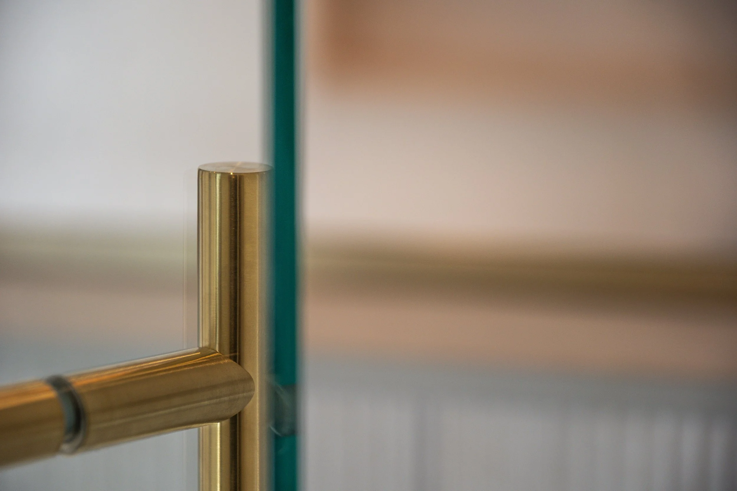 Close-up of a gold-colored metal railing with a vertical glass panel in the foreground, blurred background.