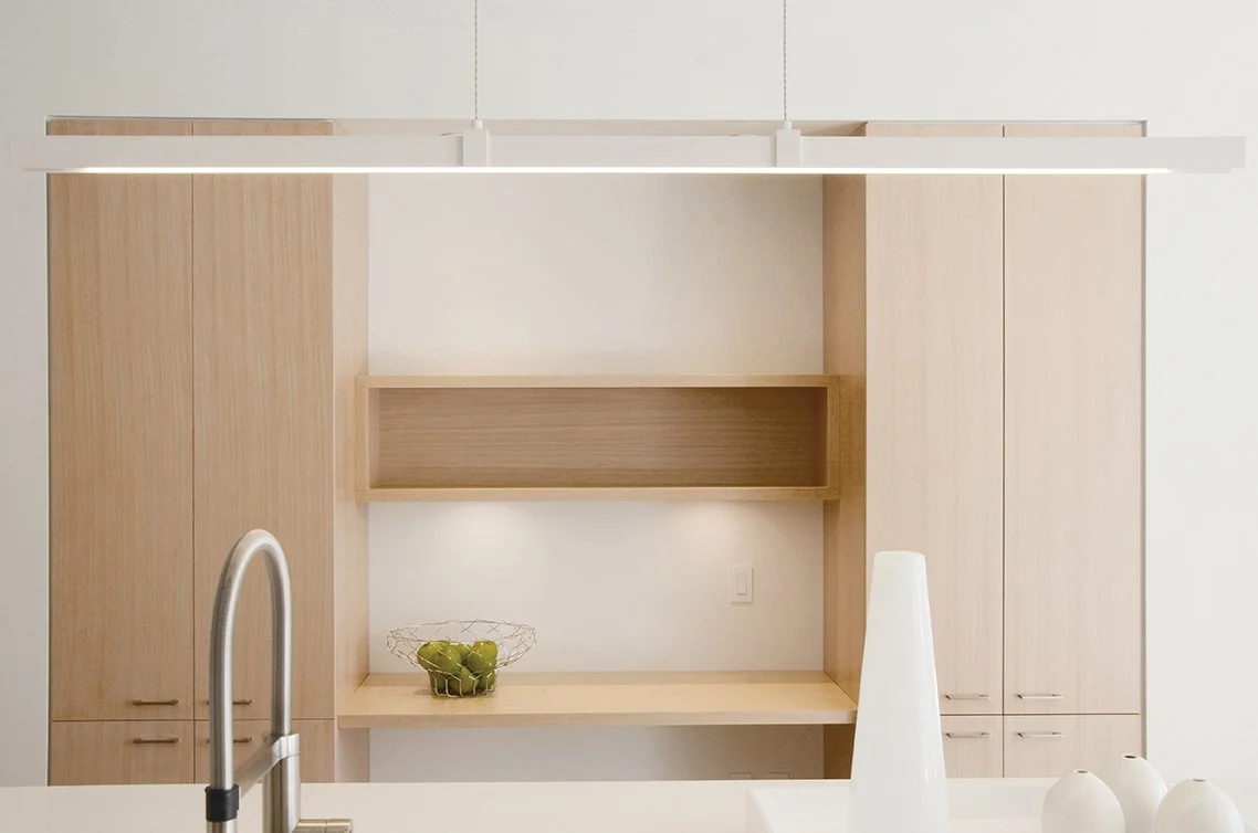 Modern kitchen with light wood cabinets, open shelves, and white walls. A fruit bowl with green apples is on the counter.