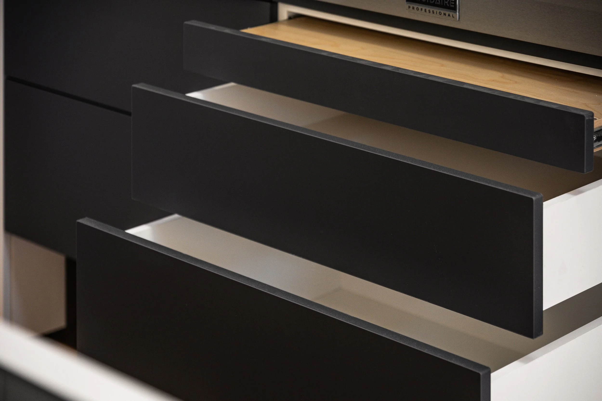 Open drawers in a modern storage unit, with some showing a black finish and one showing a wood finish.