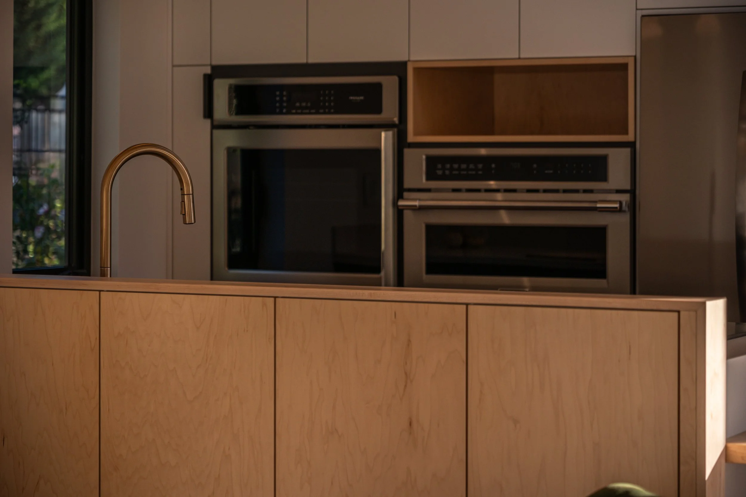 Modern kitchen with a wooden island, stainless steel oven, and a gold-colored faucet.
