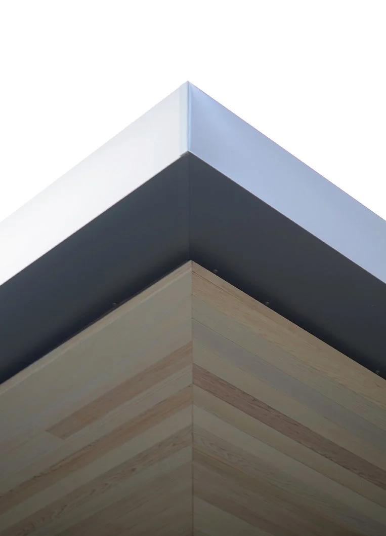 Close-up of the corner of a modern building with a white top edge, black middle section, and wooden paneling on the lower part.