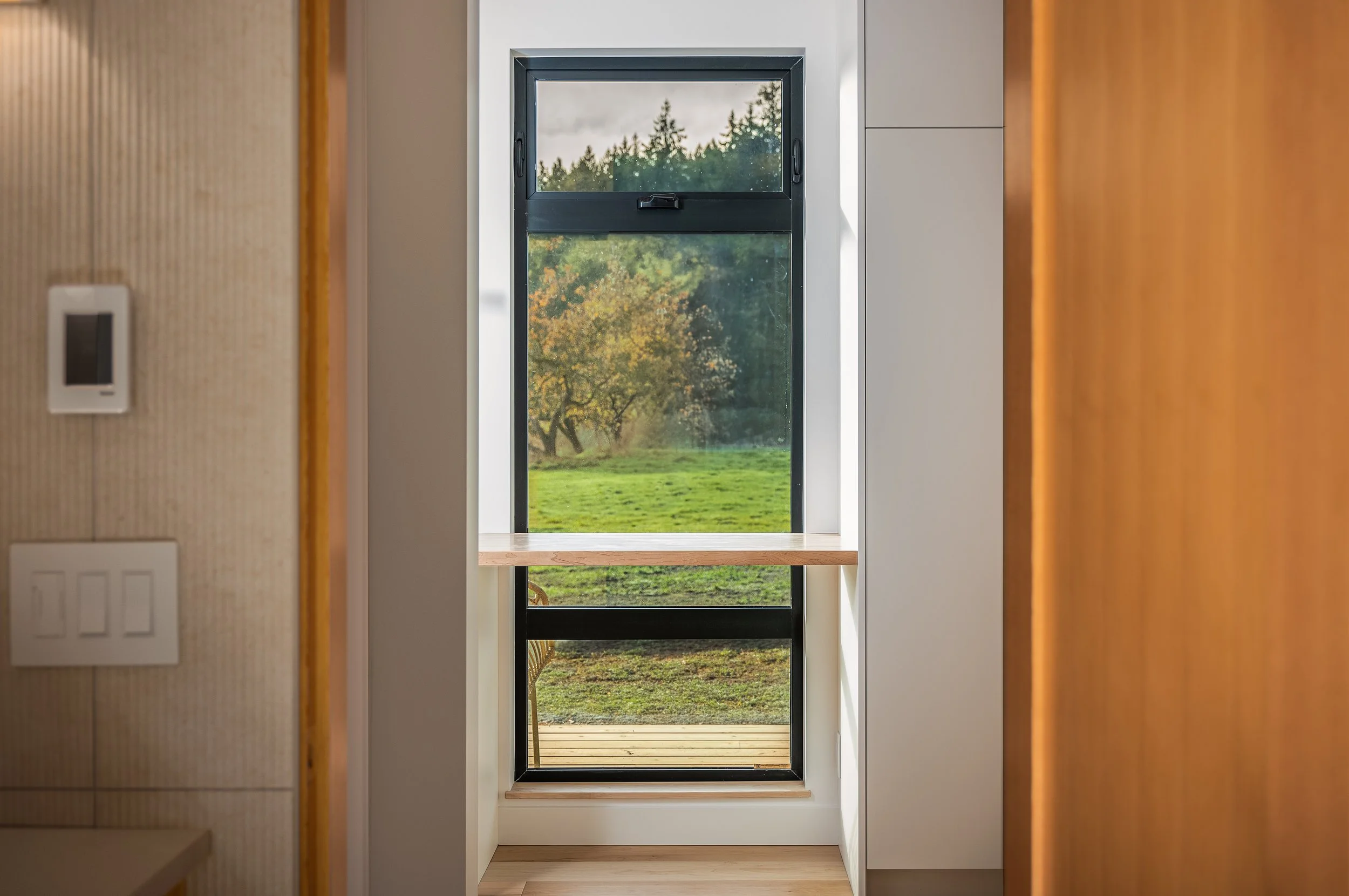 Interior view of a window with a wooden shelf, looking out onto a grassy landscape with trees in autumn colors.