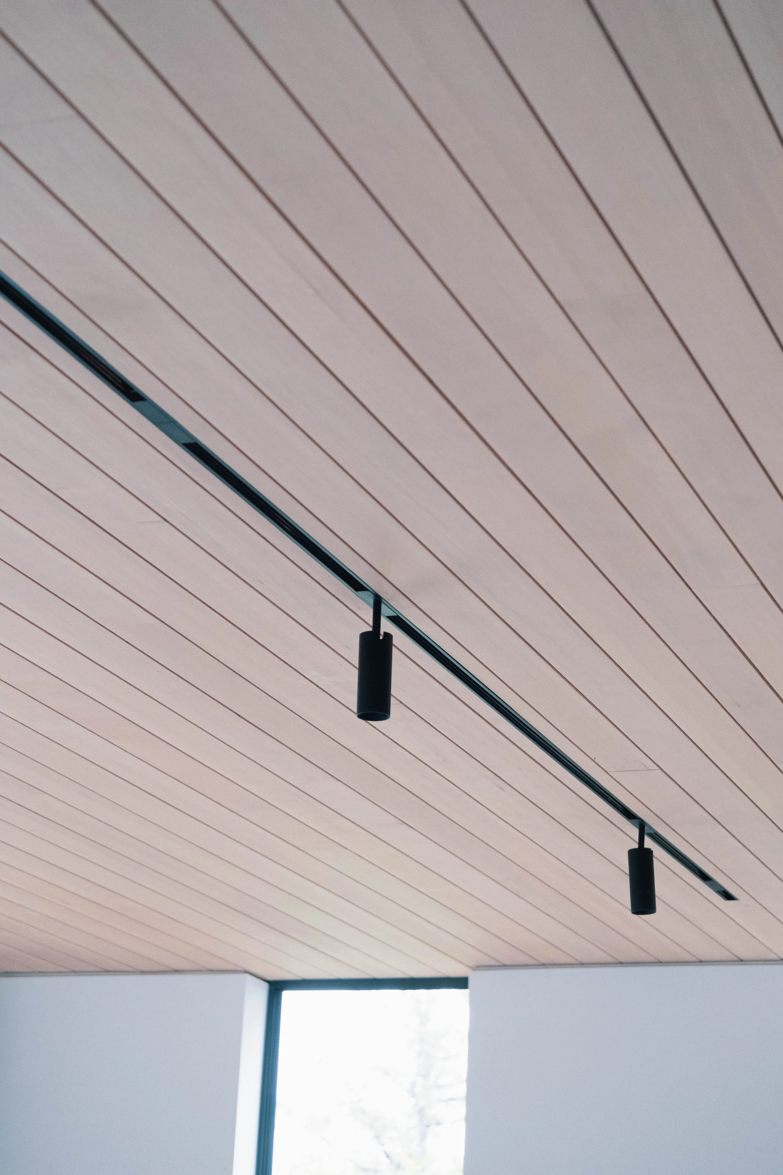 Ceiling with wooden panels and two black track lights, with a large window in the background.