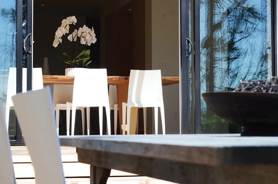 Indoor dining area with white chairs, a wooden table, and a potted white orchid plant.