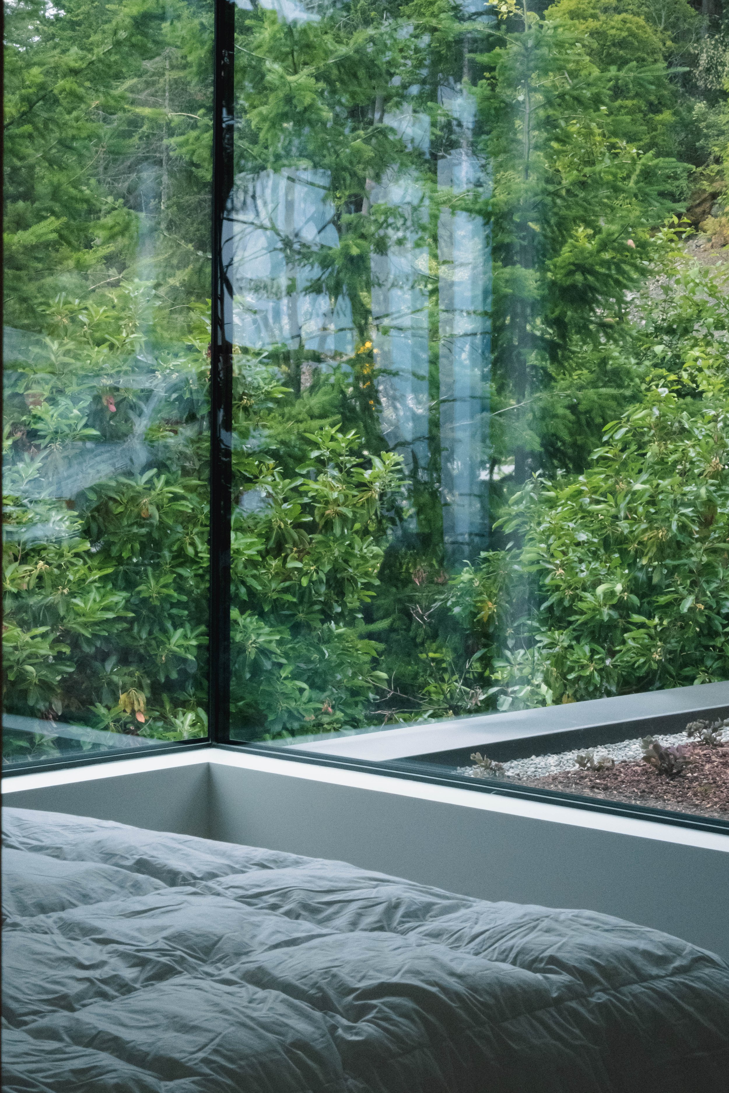 A bedroom with a bed near a large glass window showing green trees outside.
