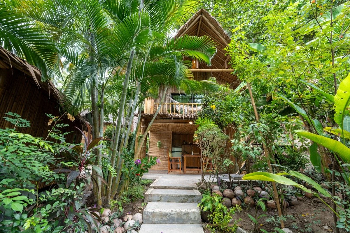 A tropical treehouse surrounded by lush greenery with a stone pathway leading to the entrance.