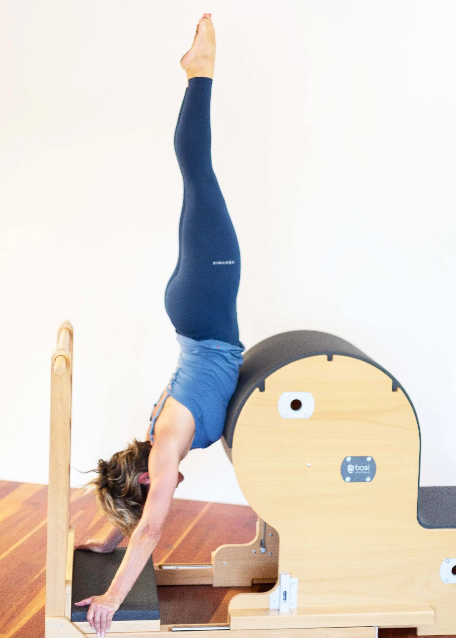 Theo Botha performing a handstand on a Pilates reformer machine in a fitness studio.