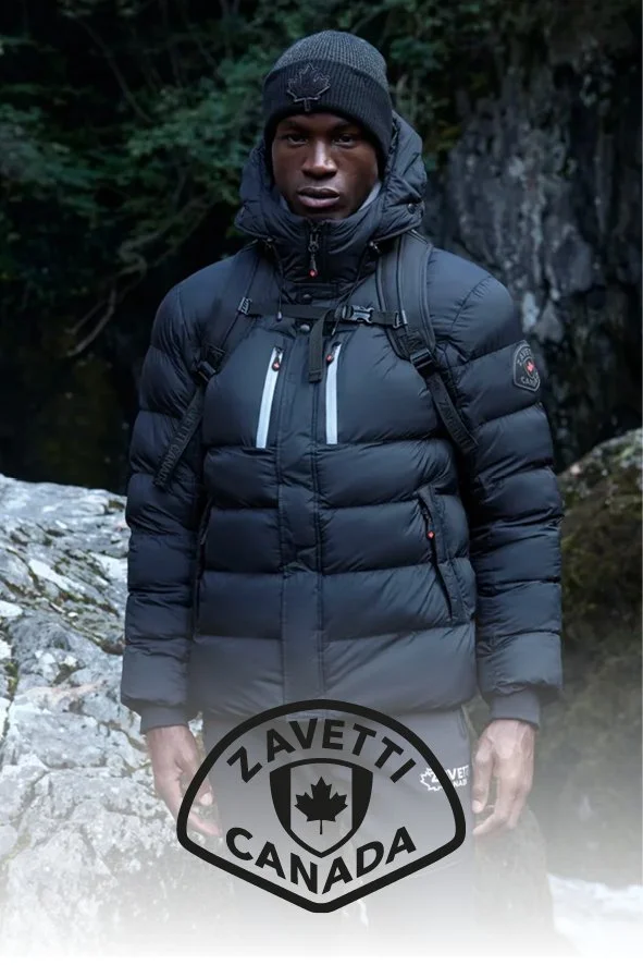 Junger Mann in dunkler, warmer Outdoor-Bekleidung mit Rucksack, standing vor Naturkulisse mit Bäumen und Felsen, ZAVETTI CANADA Logo am Bildrand.