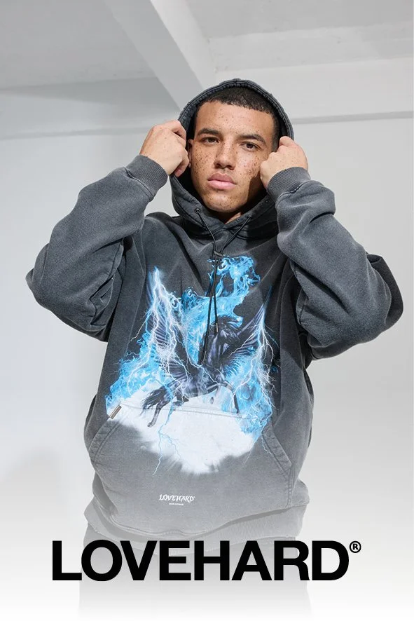 Junge trägt eine dunkle Hoodie mit einem blauen und weißen Blitz-Design, steht in einem weißen Raum, hält die Kapuze, darunter steht LOVEHARD.