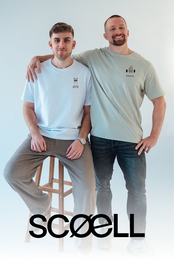 Zwei Männer stehen nebeneinander vor weißem Hintergrund, einer sitzt auf einem Hocker, beide tragen T-Shirts mit logos, eines mit einem Filzstift, das andere mit einem Hammerkzeug, und lächeln.