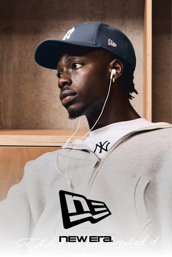 Ein junger Mann trägt eine Baseballkappe, ein Kopfhörer und ein weißes Sweatshirt mit dem New York Yankees Logo. Er sitzt in einem Raum mit Holzwand. Das Bild ist ein Werbeplakat für New Era, mit dem Slogan "we did it. we just unleashed it."