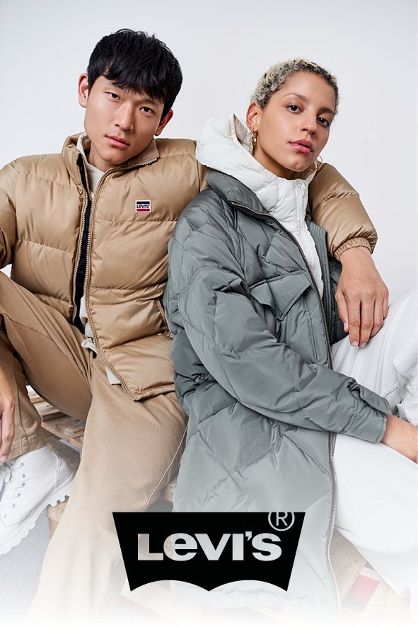Zwei junge Erwachsene sitzen nebeneinander, tragen lässige Winterjacken, eine beige, die andere grau, und schauen in die Kamera, gegen einen weißen Hintergrund. Das Levi's-Logo ist sichtbar im unteren Bereich des Bildes.
