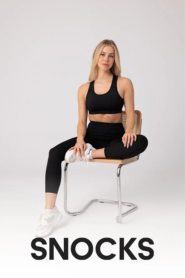 Junge Frau in sportlicher Kleidung sitzt auf einem Stuhl, kreuzt die Beine und hat eine White Sneakers an. Der Hintergrund ist weiß. Das Wort "SNACKS" ist unten im Bild geschrieben.