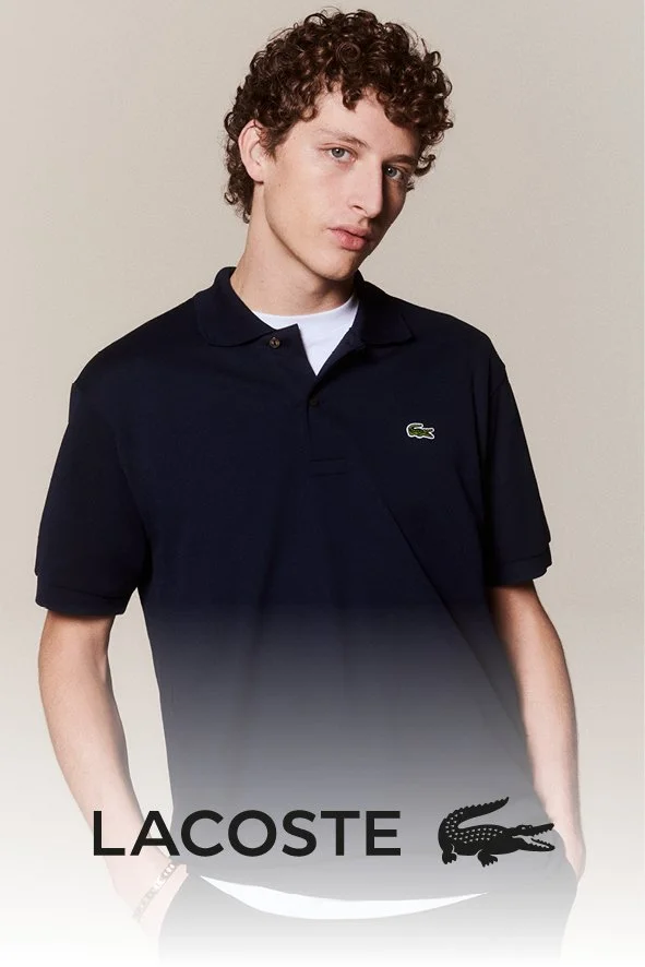 Ein junger Mann mit lockigem Haar trägt ein schwarzes Lacoste Poloshirt mit Logo auf der Brust, gegen einen neutralen Hintergrund.