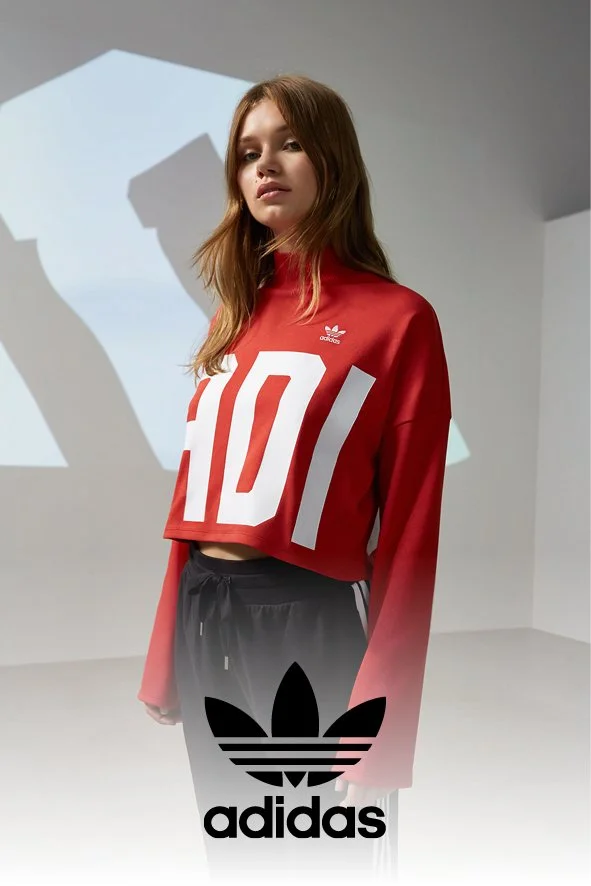 Junge Frau in rotem Adidas-Sporttop und schwarzen Adidas-Hosen in einem weißen Raum, Hintergrundprojektion, Adidas-Logo sichtbar.