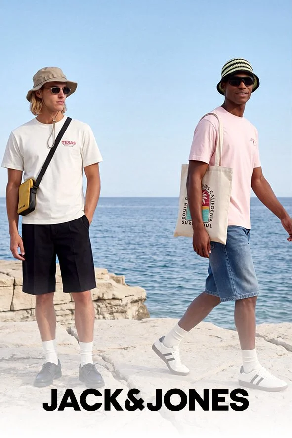 Zwei junge Menschen stehen am Meer, tragen Sonnenhüte, Sonnenbrillen und casual Kleidung, eine Person hat eine Tasche mit "California Surf" Aufdruck, die andere eine schwarze Umhängetasche, im Hintergrund blauer Himmel und Meer.