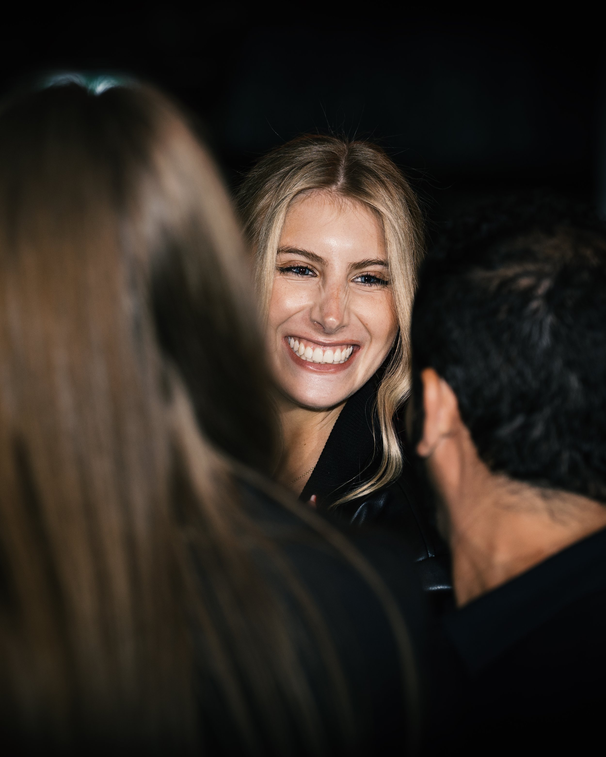 A blonde woman with a big smile talking with two other people whose faces are not visible.
