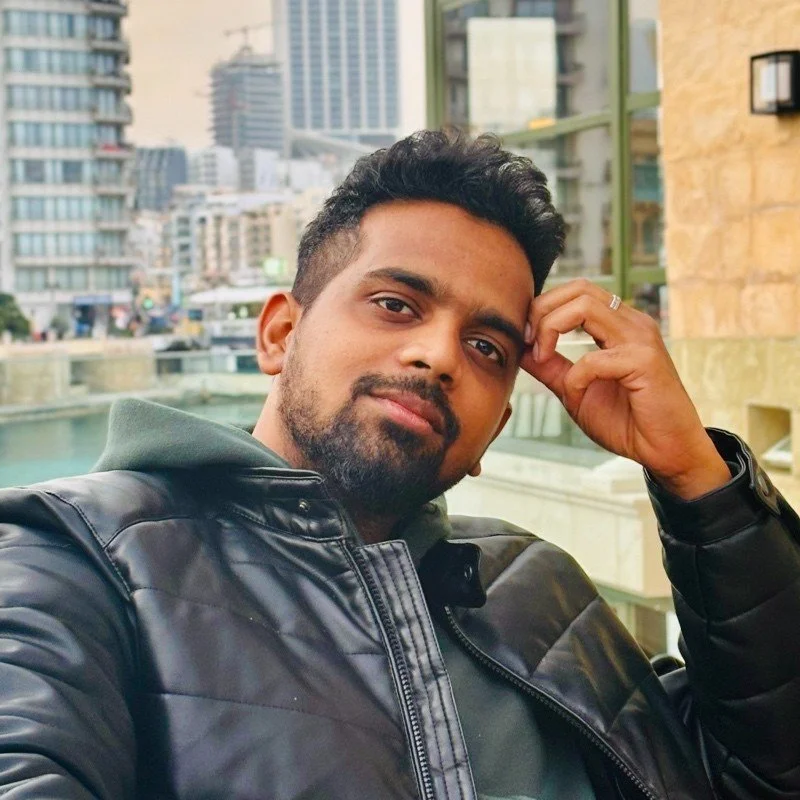 Person in a black leather jacket posing outdoors with a city skyline in the background.