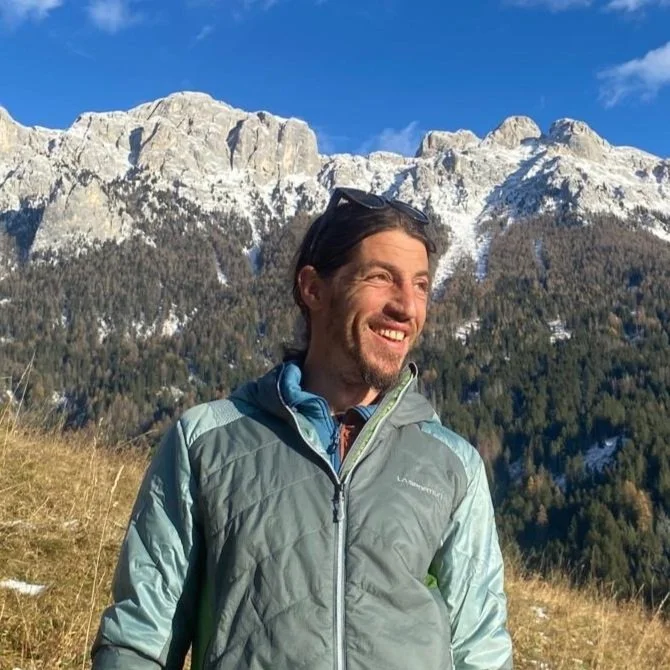 Man kneeling and smiling with two dogs on leashes in a parking lot.