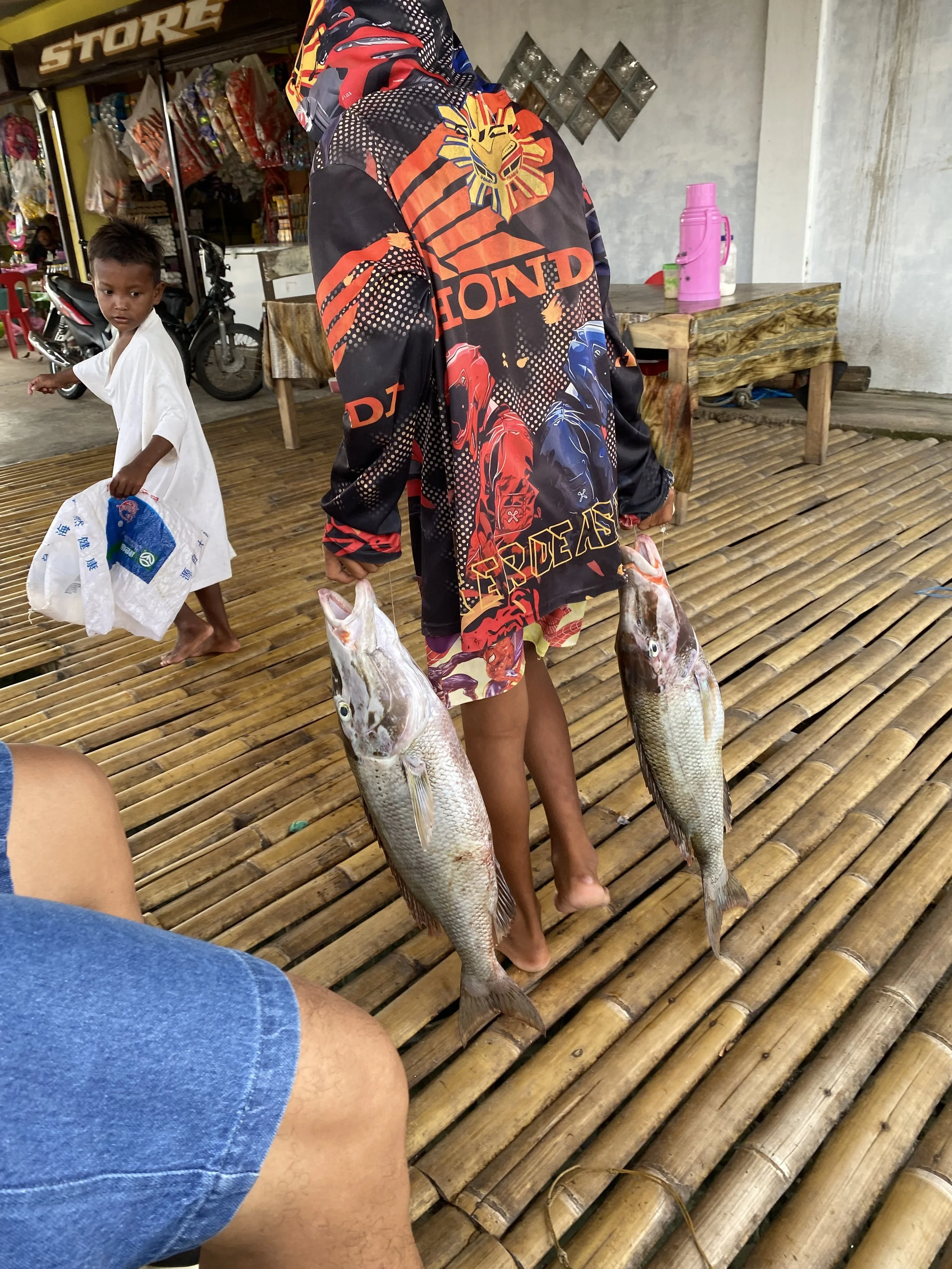 A fisherman carries two large freshly caught fish across a bamboo floor on Simunul Island in Tawi-Tawi, Philippines.