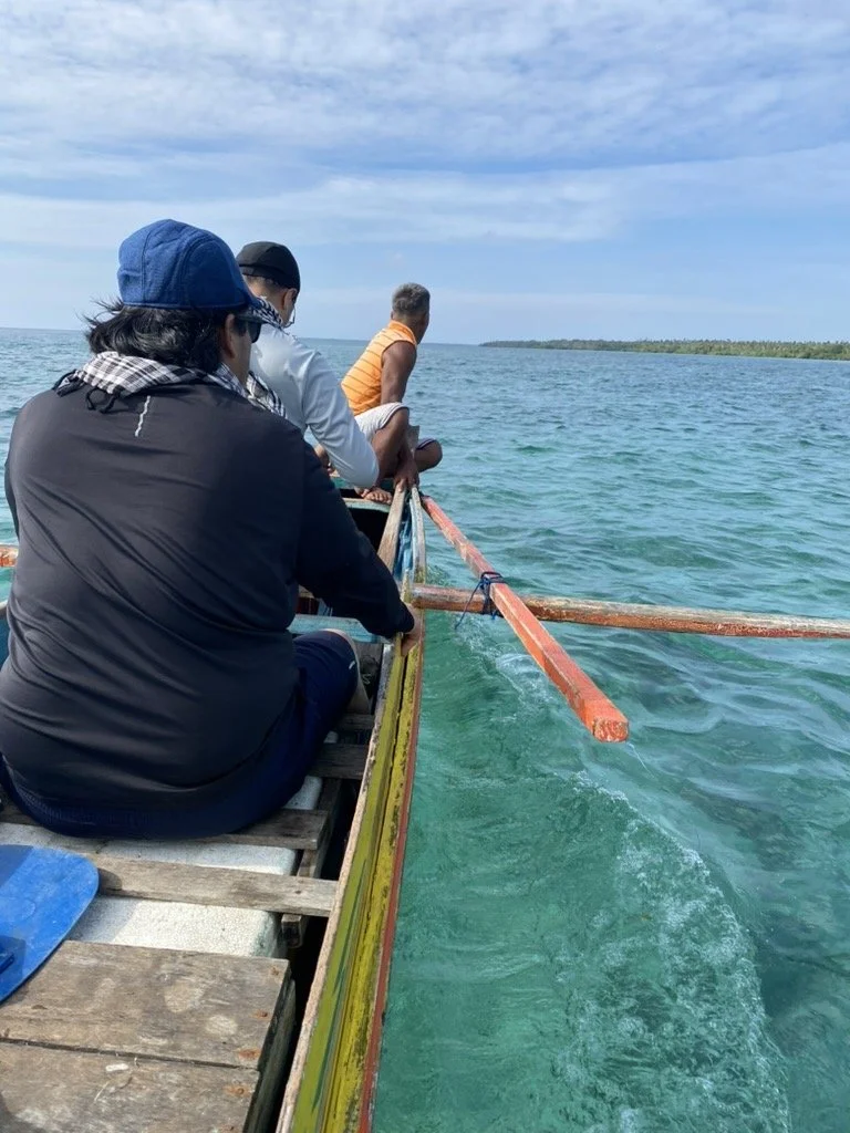 Passengers ride in a small wooden outrigger boat across turquoise water near Simunul Island in Tawi-Tawi, Philippines, with a low green island ahead.