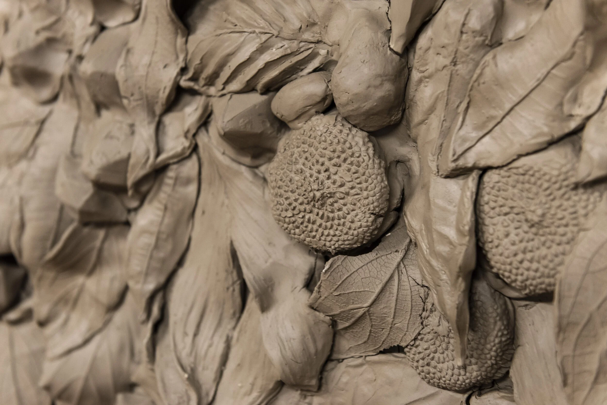 Close-up of a clay sculpture depicting strawberries, leaves, and textured flowers.