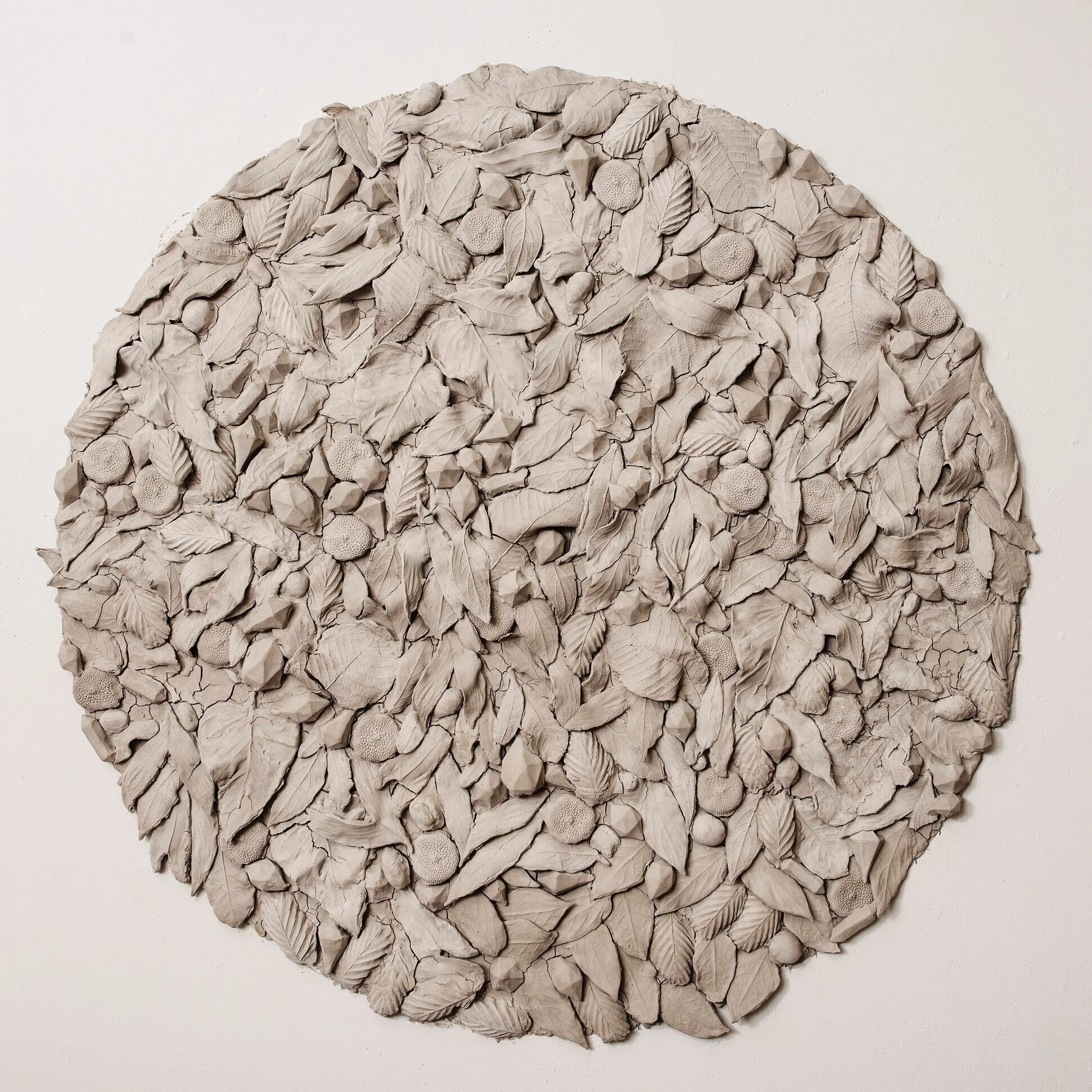 Round wall sculpture made of beige fabric leaves, berries, and textured elements.