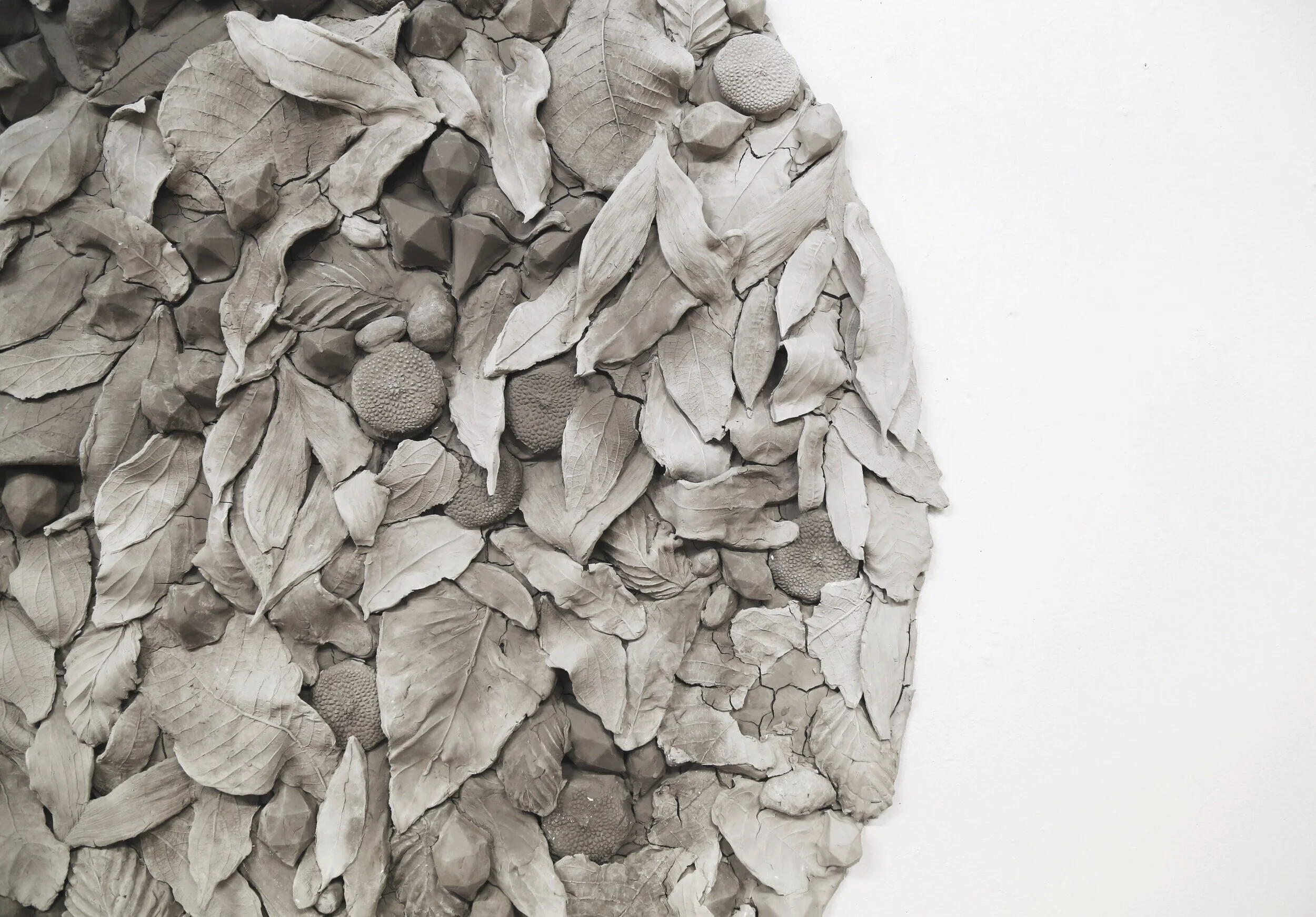 A monochrome sculpture made of clay depicting an arrangement of leaves, berries, and flowers.
