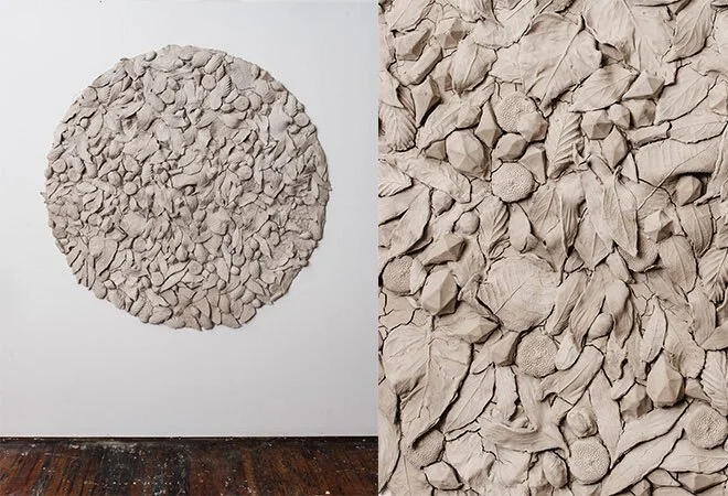 Artwork featuring a circular arrangement of textured, paper-like material resembling crumpled and torn paper or clay on a white wall in an art gallery.