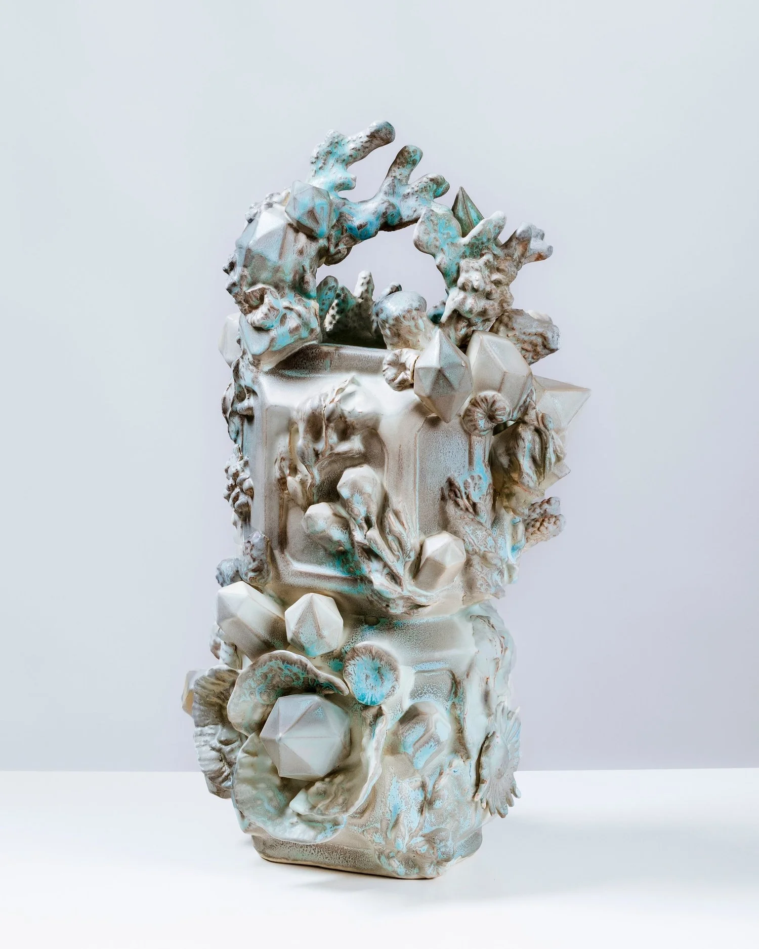 A vertical, off white ceramic vessel with botanical motifs, coral, gems, and marine textures with an ombre blue glazing treatment.