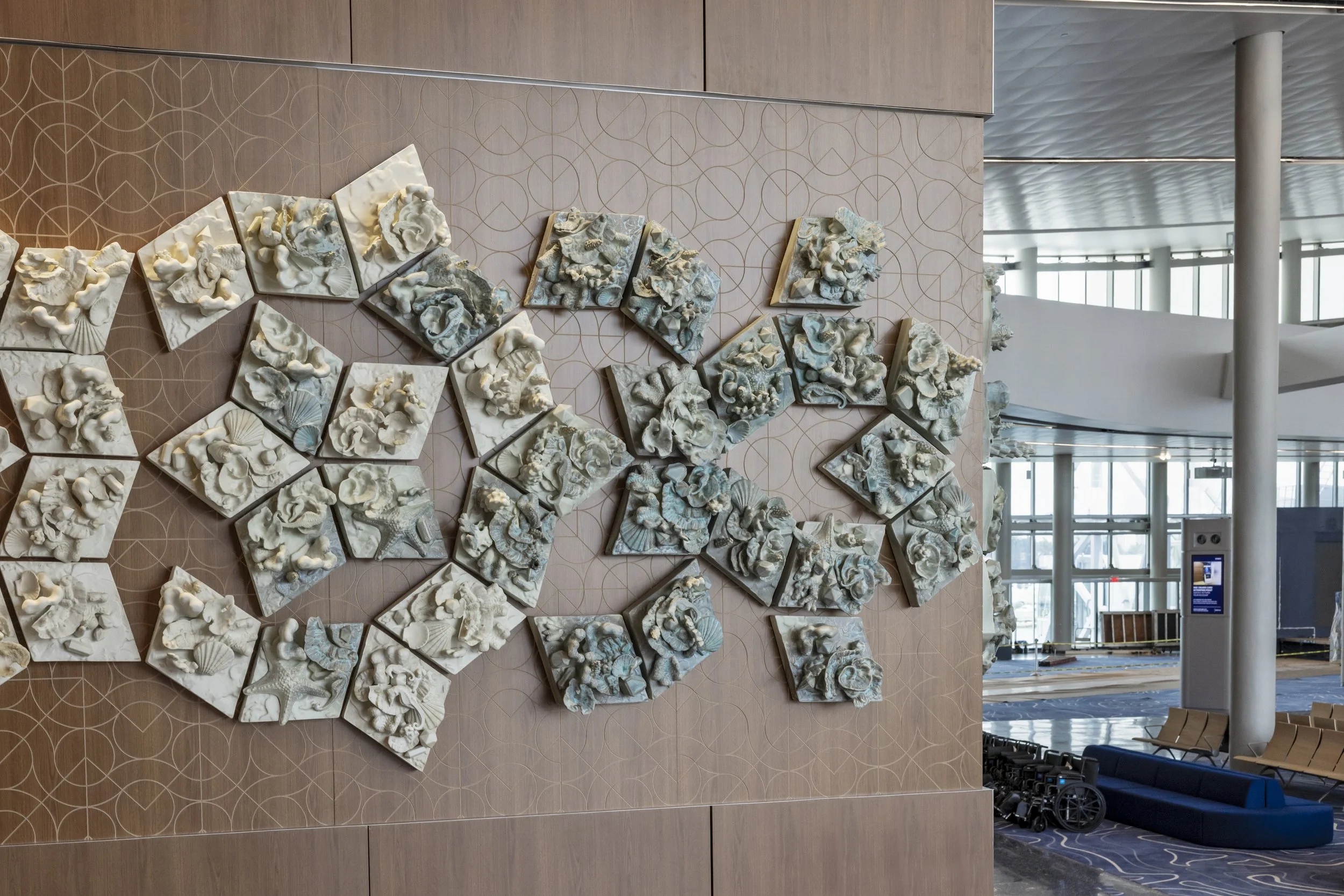 A large scale ceramic wall installation of individually cast relief tiles arranged in a dynamic, tessellated formation. Each Tile carries intricate textures and organic motifs inspired by coral, shells, and ecological patterns.
