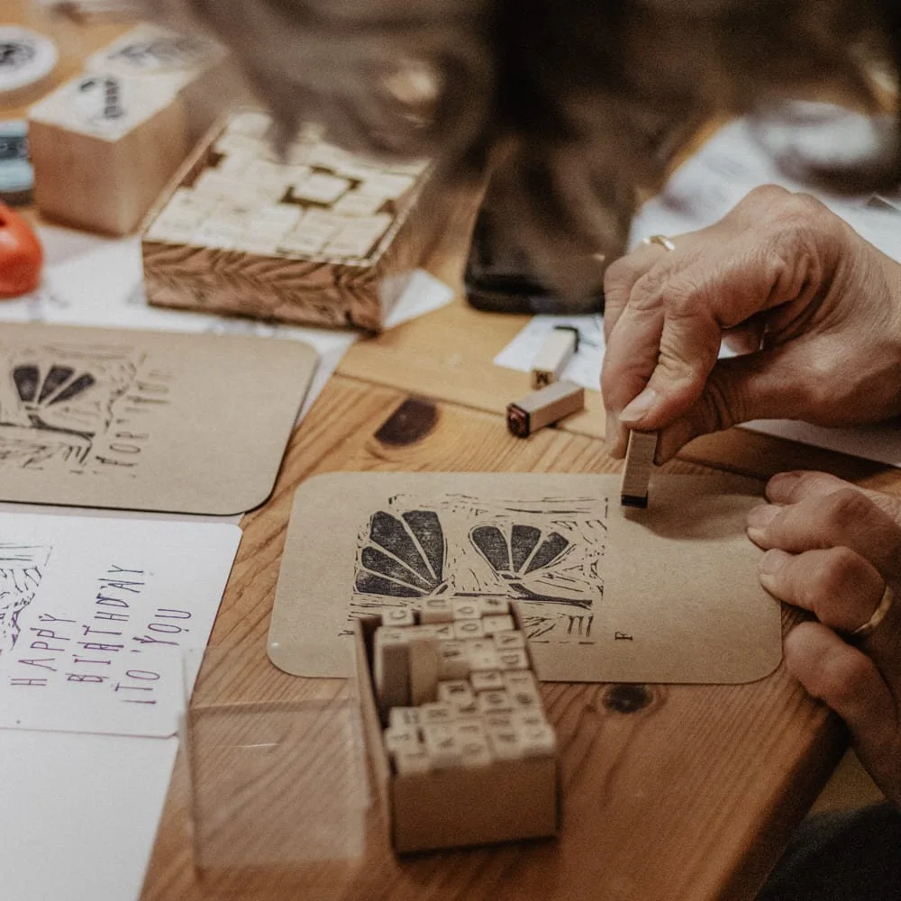Workshop-Teilnehmerin stempelt unter ihr gedrucktes Motiv mit Buchstaben das Wort "Flowers"