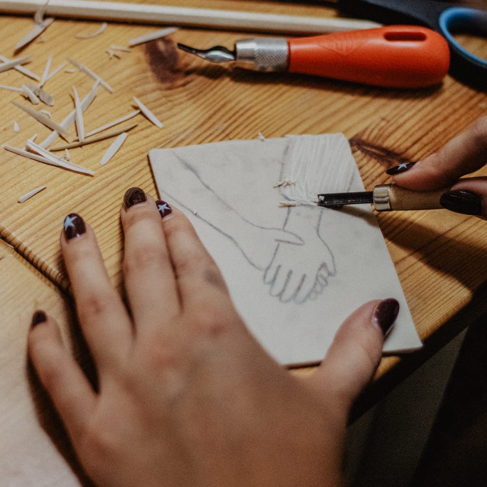 Workshop-Teilnehmerin fertig eine Linoldruckplatte an, mit zwei Händen, die sich berühren