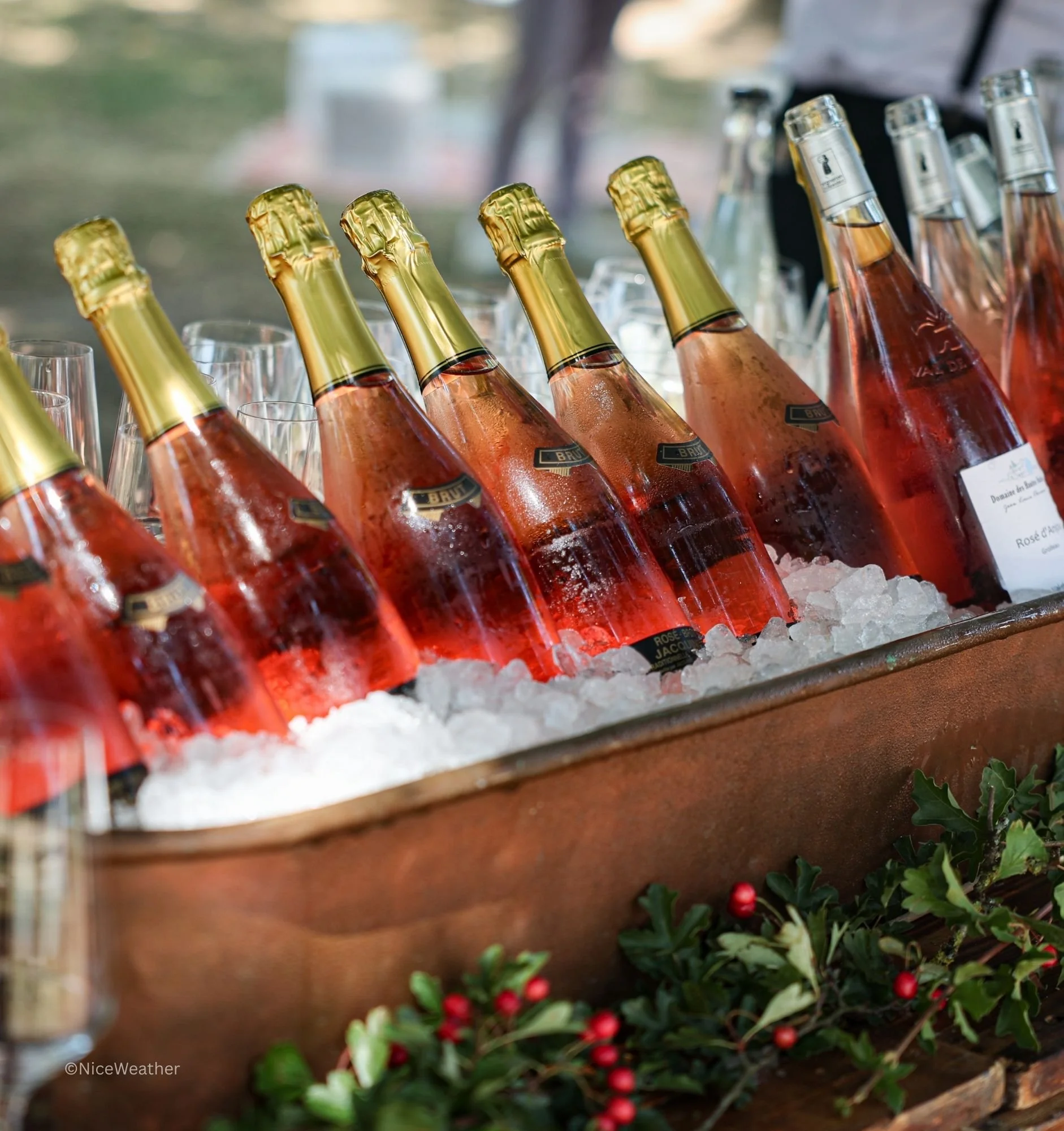 Bouteilles de champagne rosé avec étiquettes, refroidies sur de la glace dans un bac en cuivre, décoré avec des branches de houx avec des baies rouges.