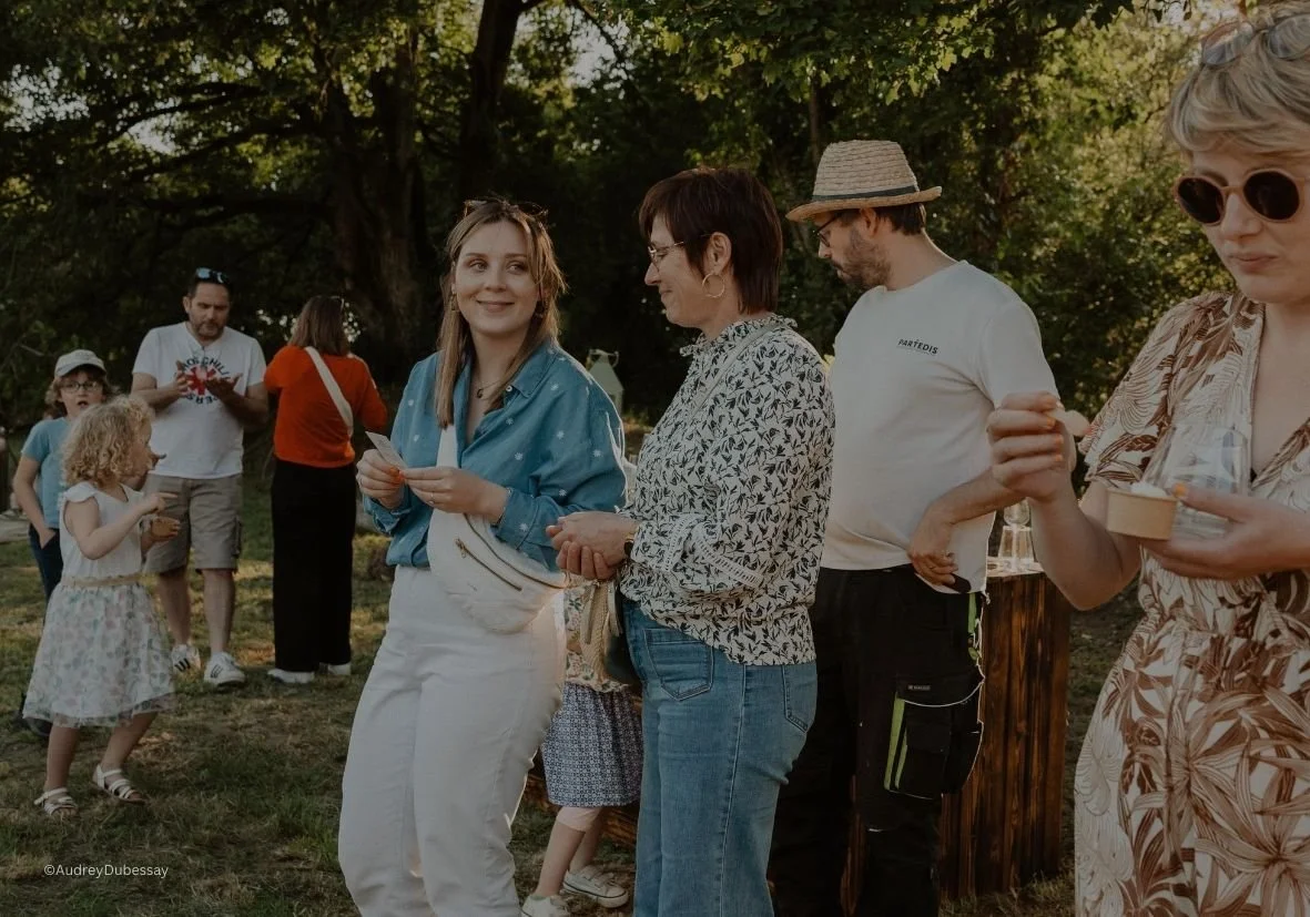 Groupe de personnes devant un fond d'arbres lors d'une fête en plein air, avec enfants, adultes, et ambiance conviviale.