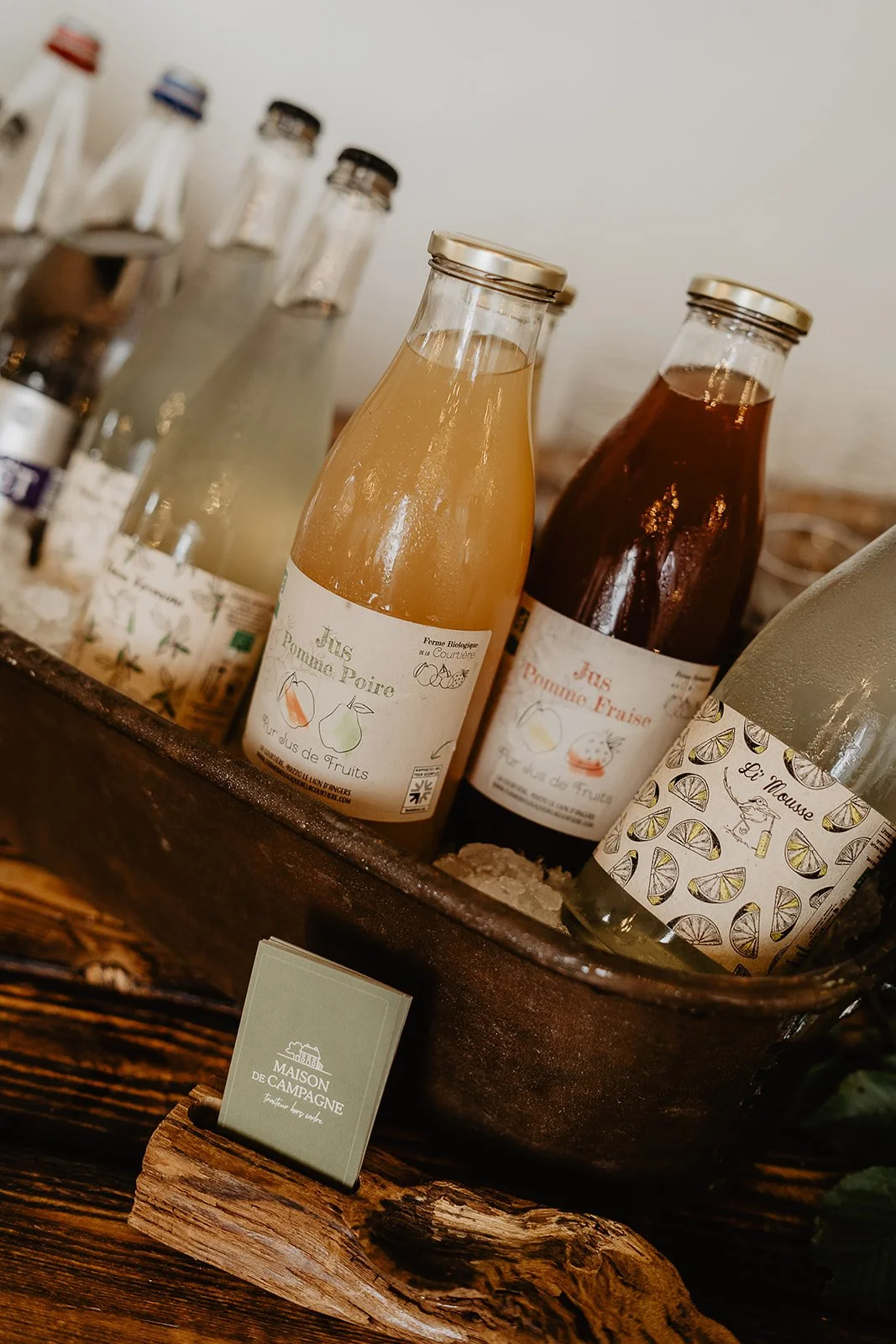 Bouteilles de sirops aux fruits biologiques dans un panier en métal, sur une table en bois.