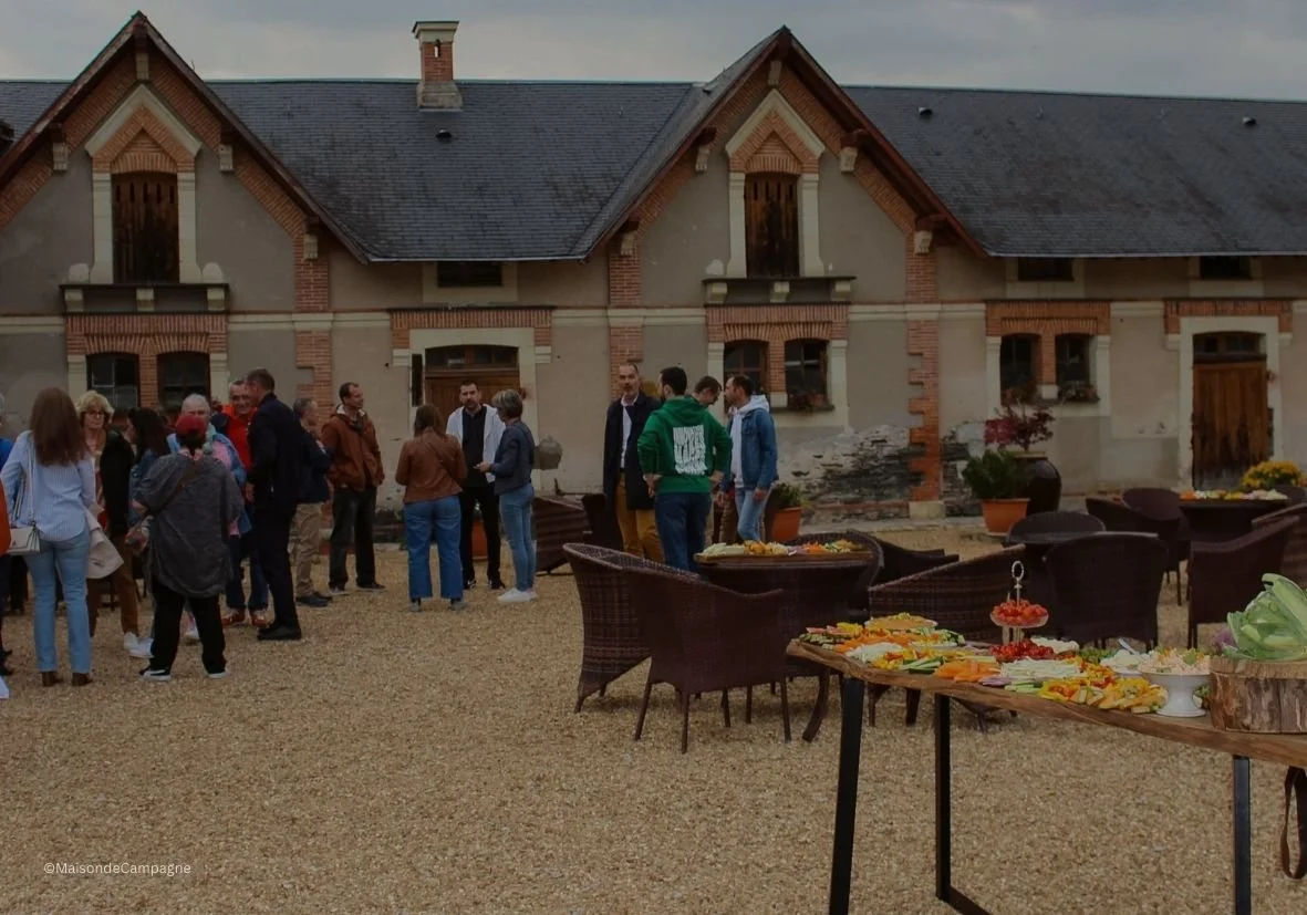 groupe de personnes dehors devant une grande maison, avec une table de nourriture devant eux.