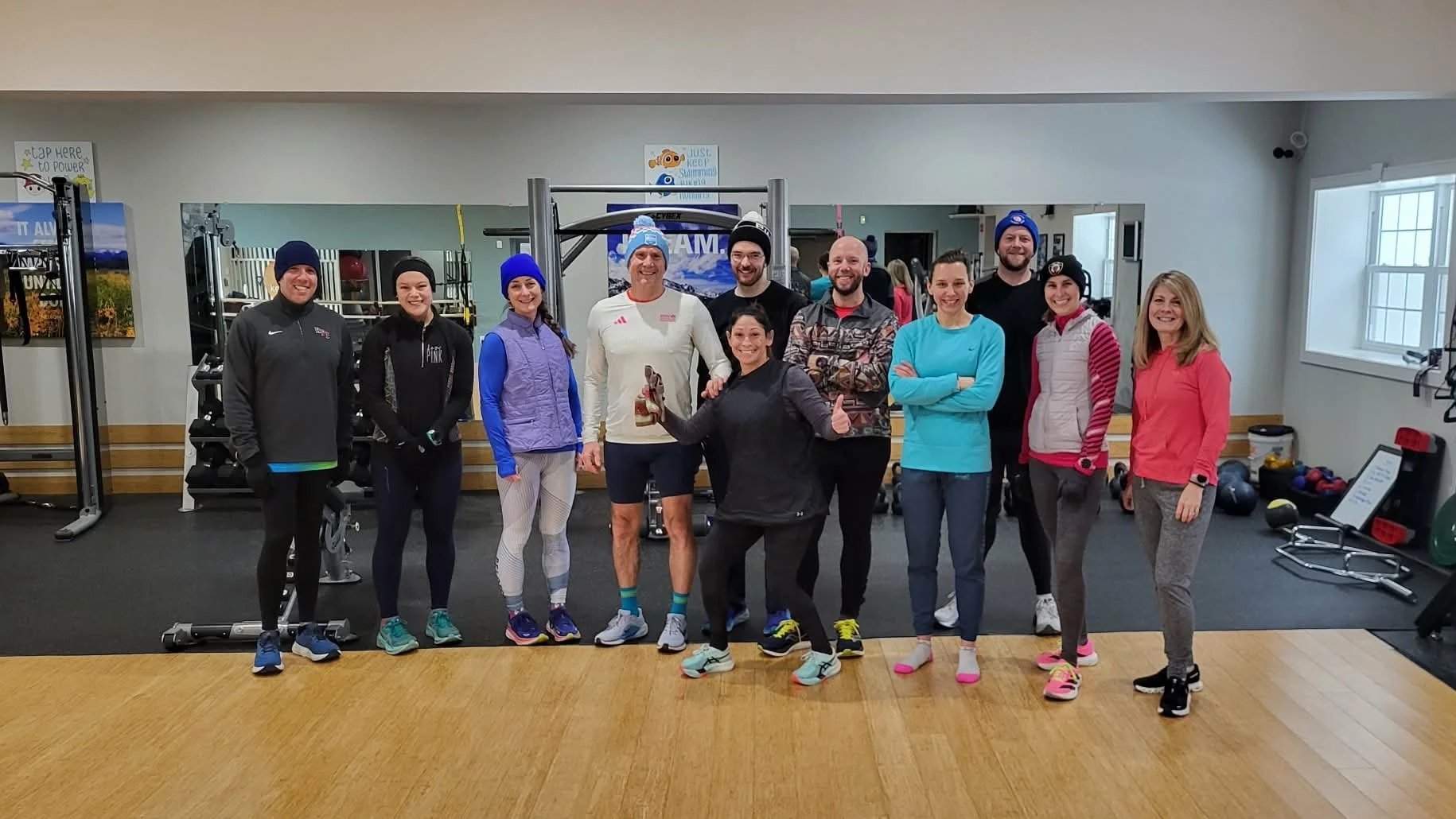 A group of ten people standing in a gym, dressed in workout attire, smiling and posing for a photo before a group long run.