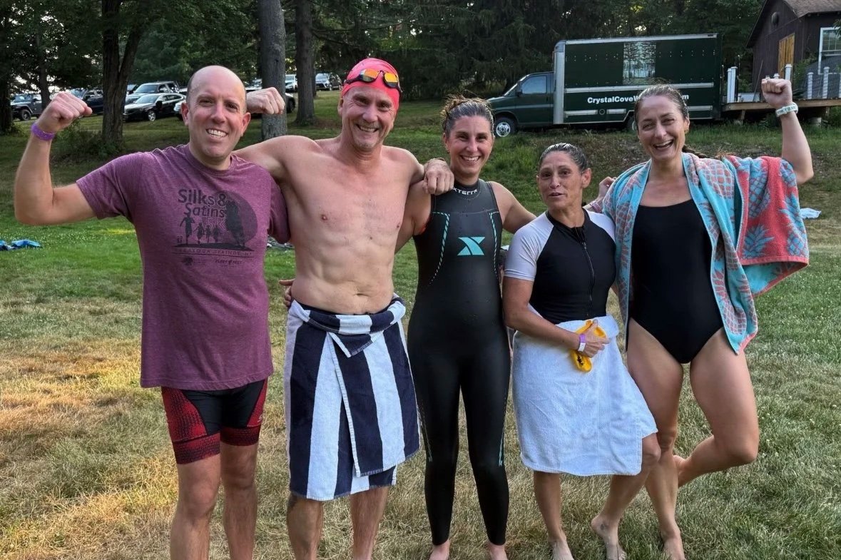 Empire State endurance athletes smiling, standing outdoors on a grassy field, celebrating after an open water swim training.