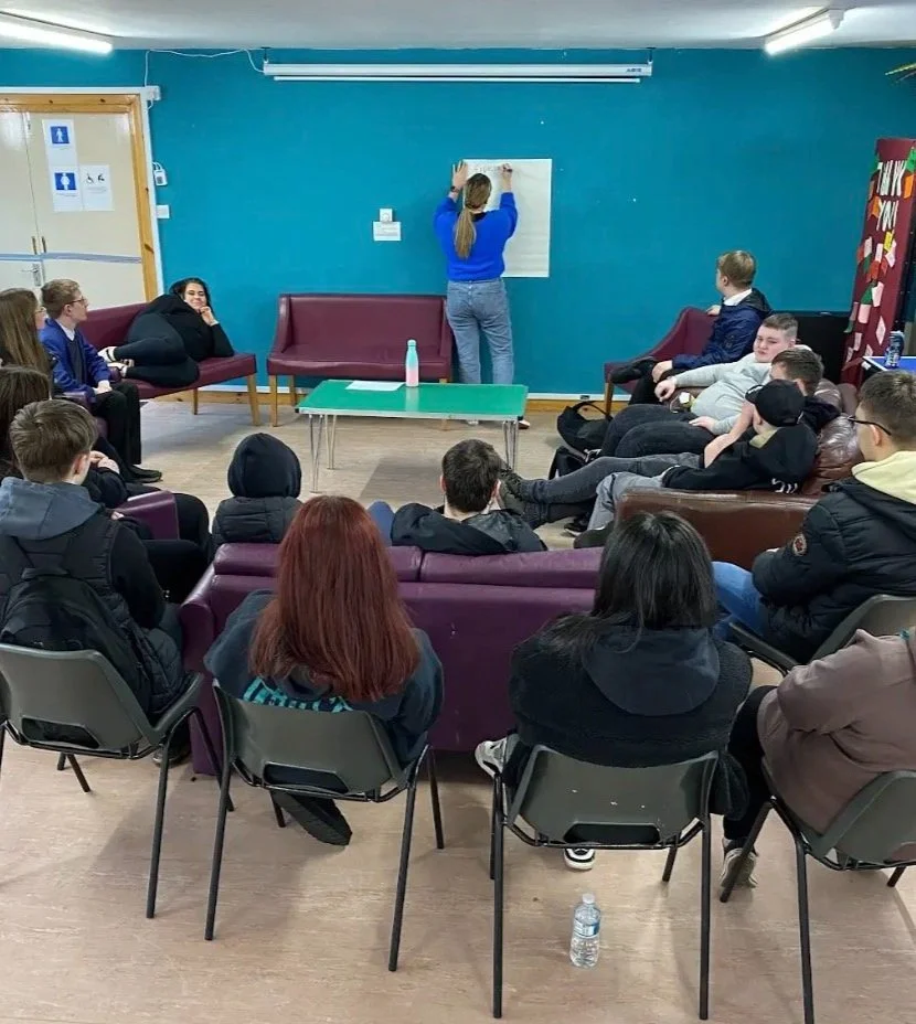 Group of people in a casual meeting room, one person writing on a flip chart.