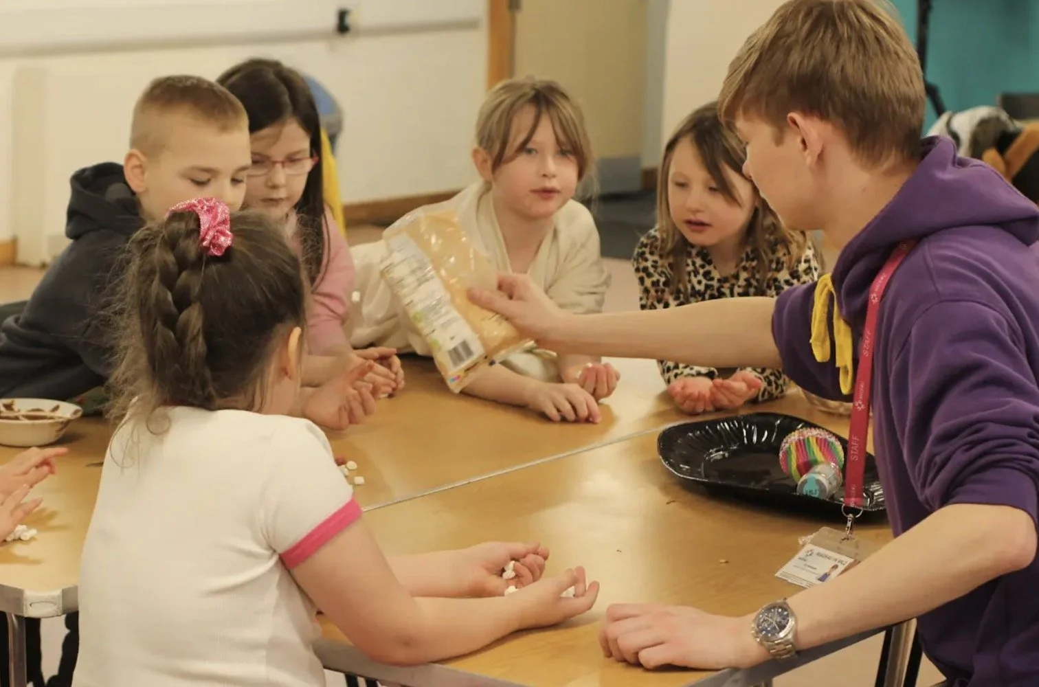 Group of children and an adult at a table engaging in a craft activity with supplies.