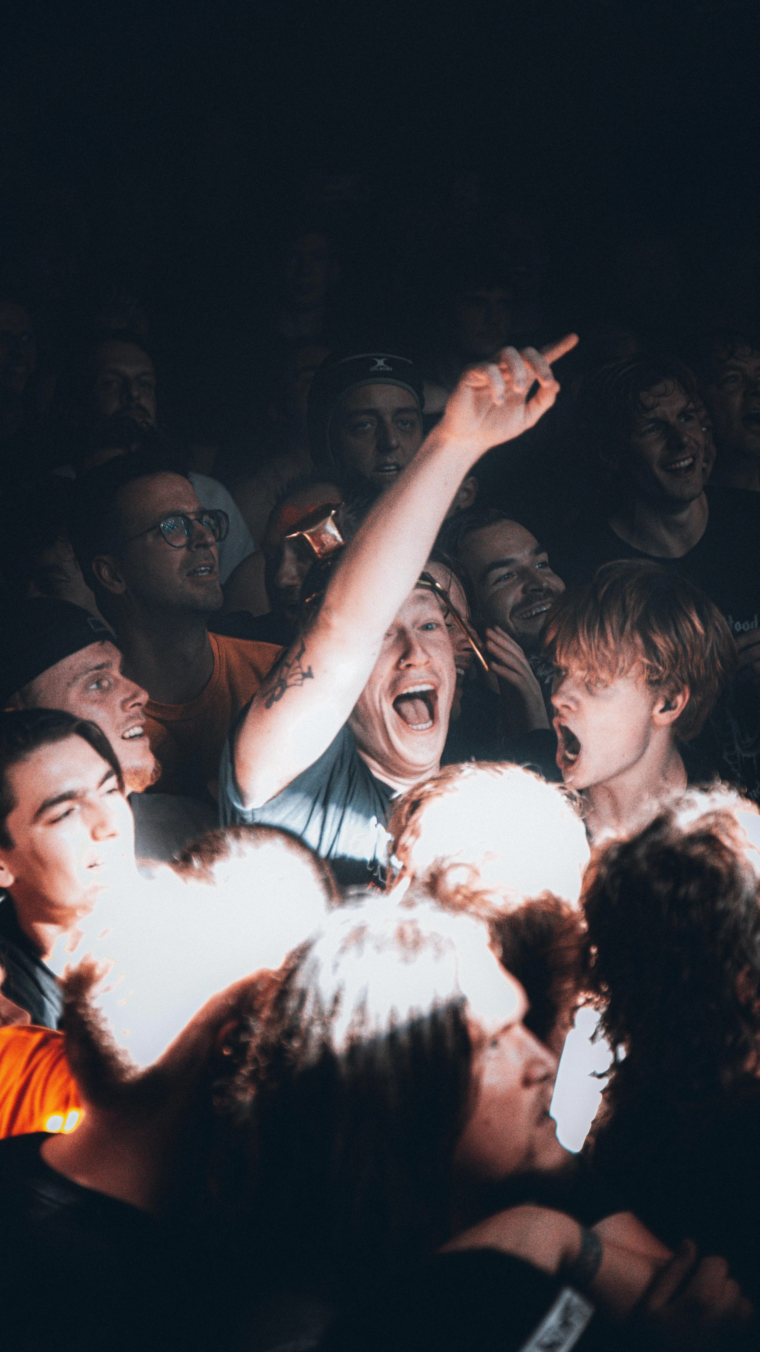 Crowd of excited people at a concert or event, some laughing and shouting, with one person raising a finger.
