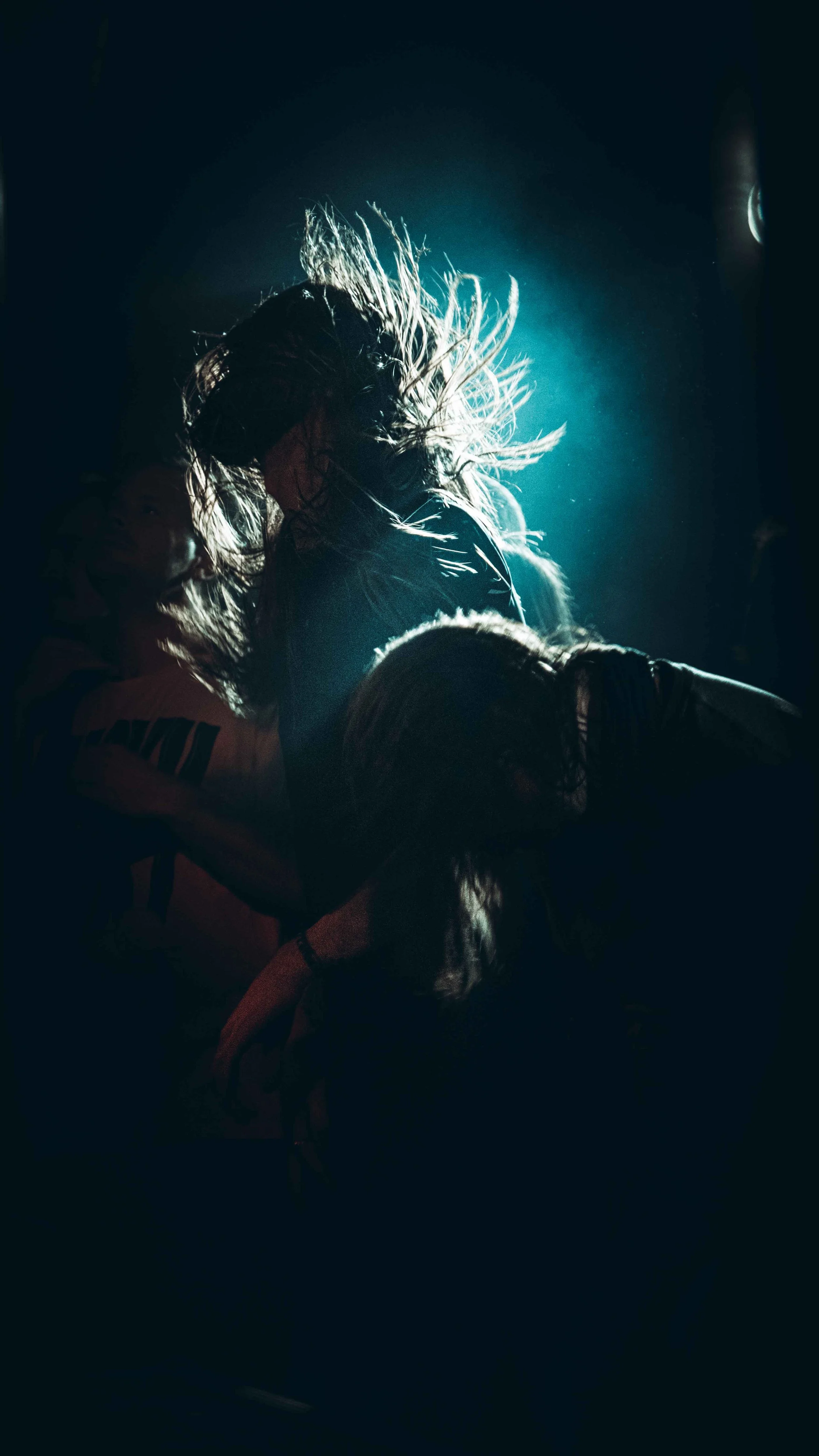 Two women dancing or wrestling in a dark setting with a blue backlight, hair flying and movement captured.