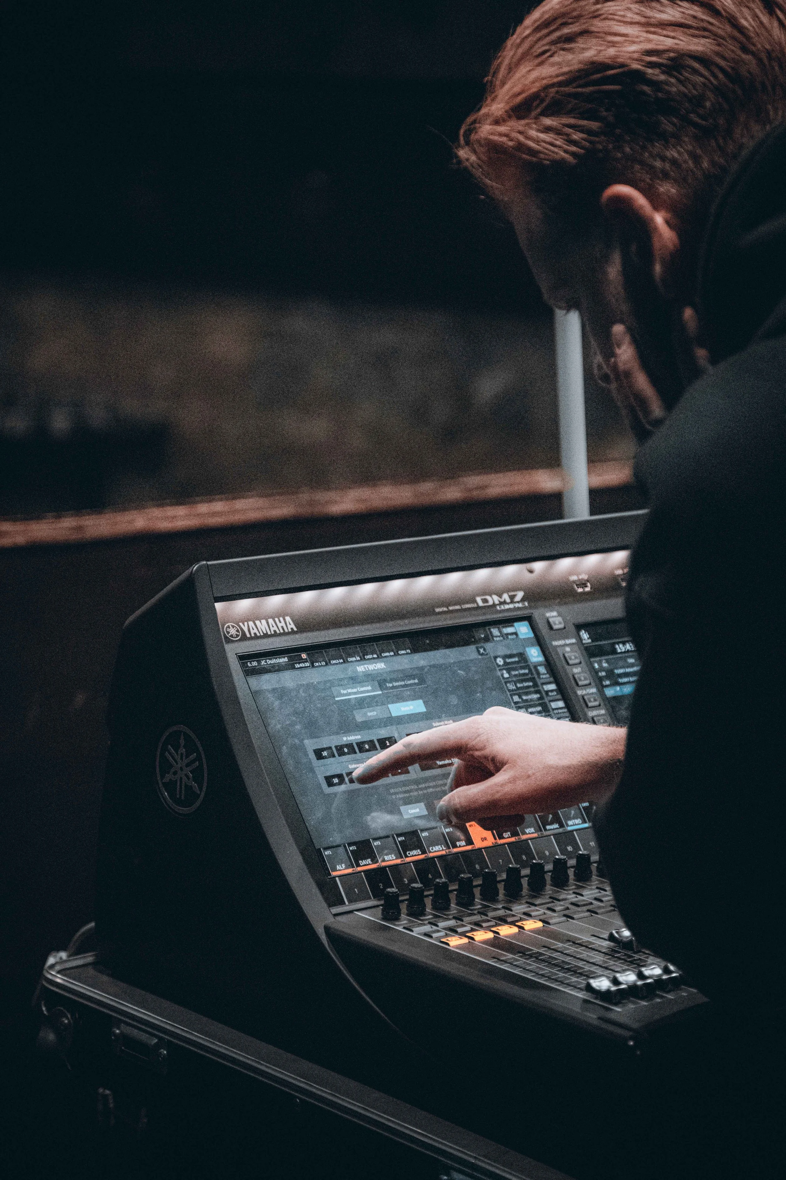 Person operating a Yamaha DM7 digital mixing console in a dimly lit environment.