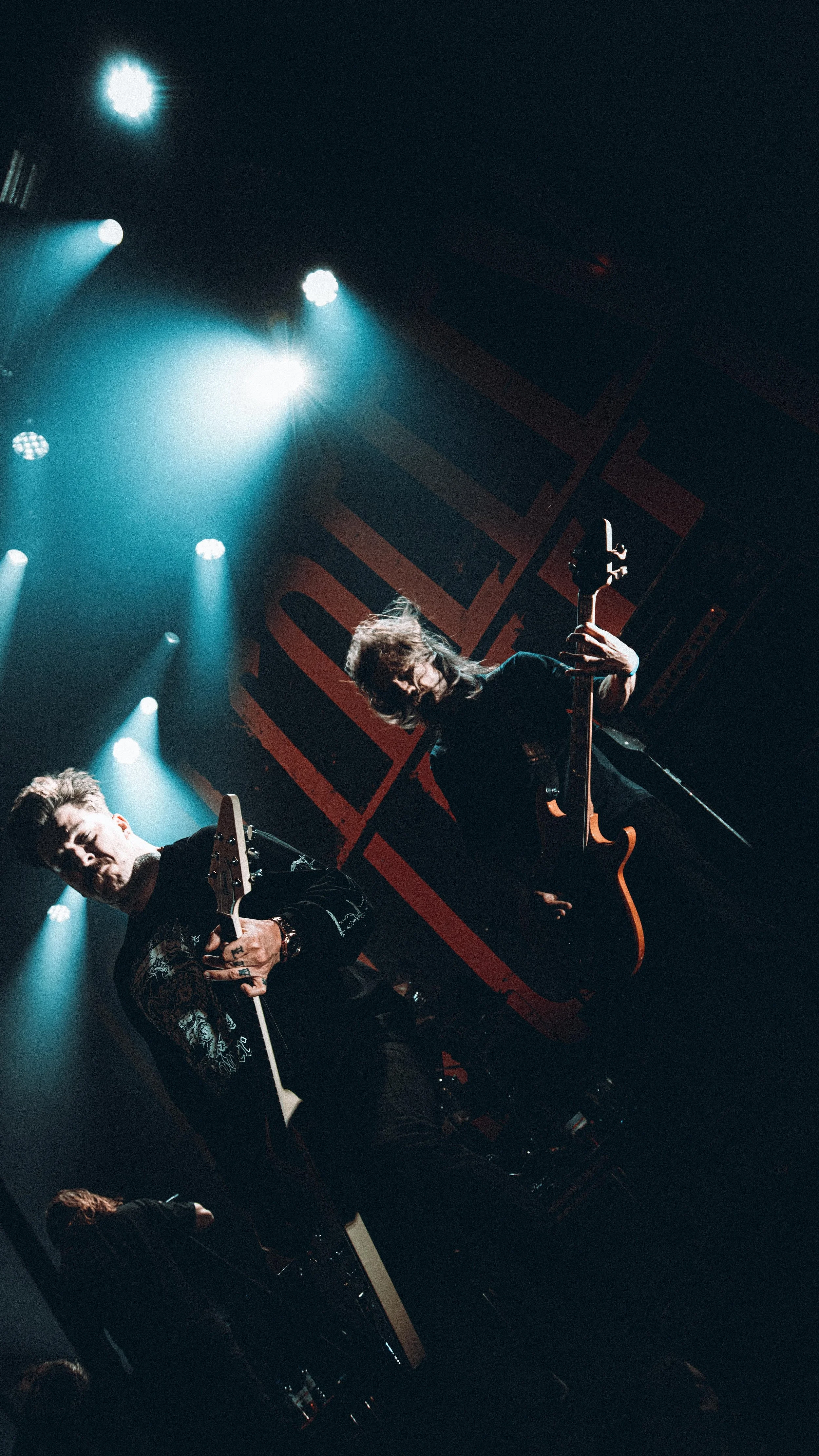 Two musicians perform on stage with guitars under bright stage lights at a concert.