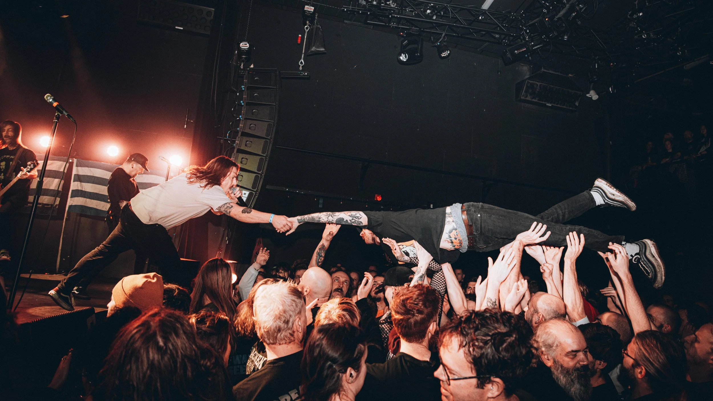 A concert scene with a band performing on stage and a crowd holding up a person in the air during a live show.