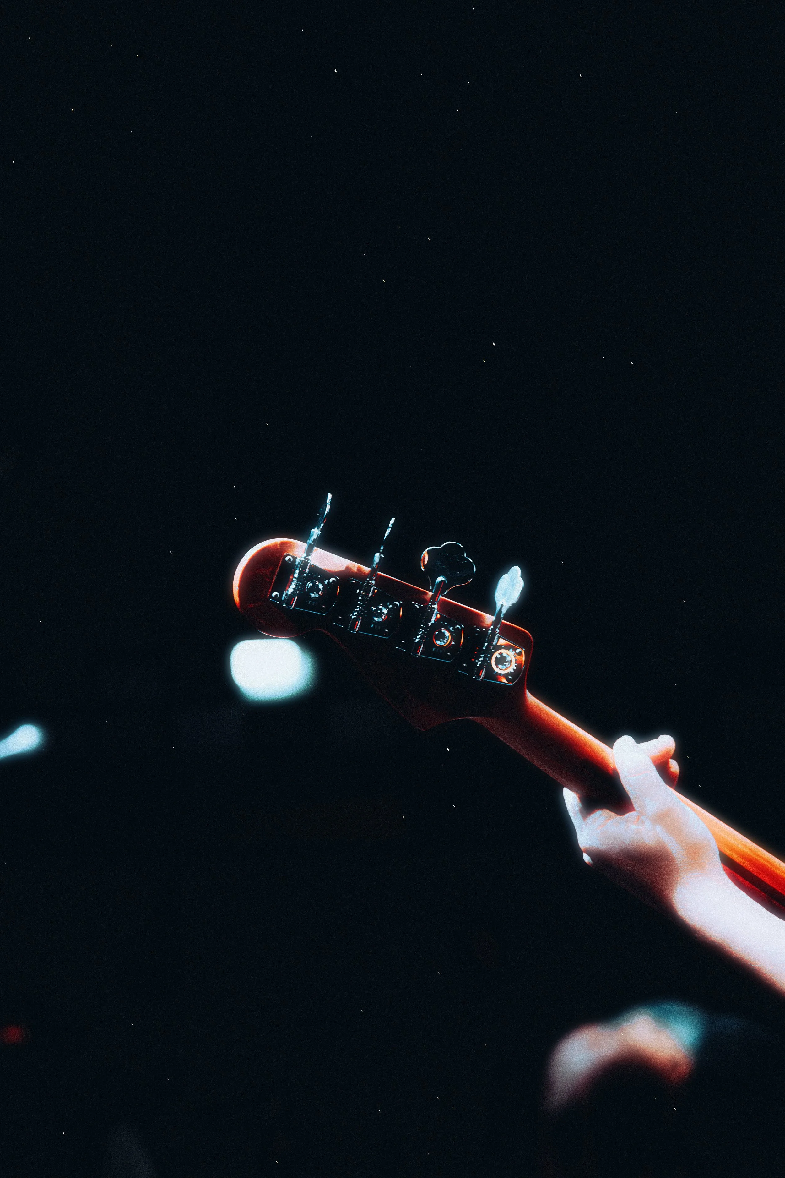 Close-up of a guitar neck and headstock against a dark background with stars, with a hand holding the guitar.