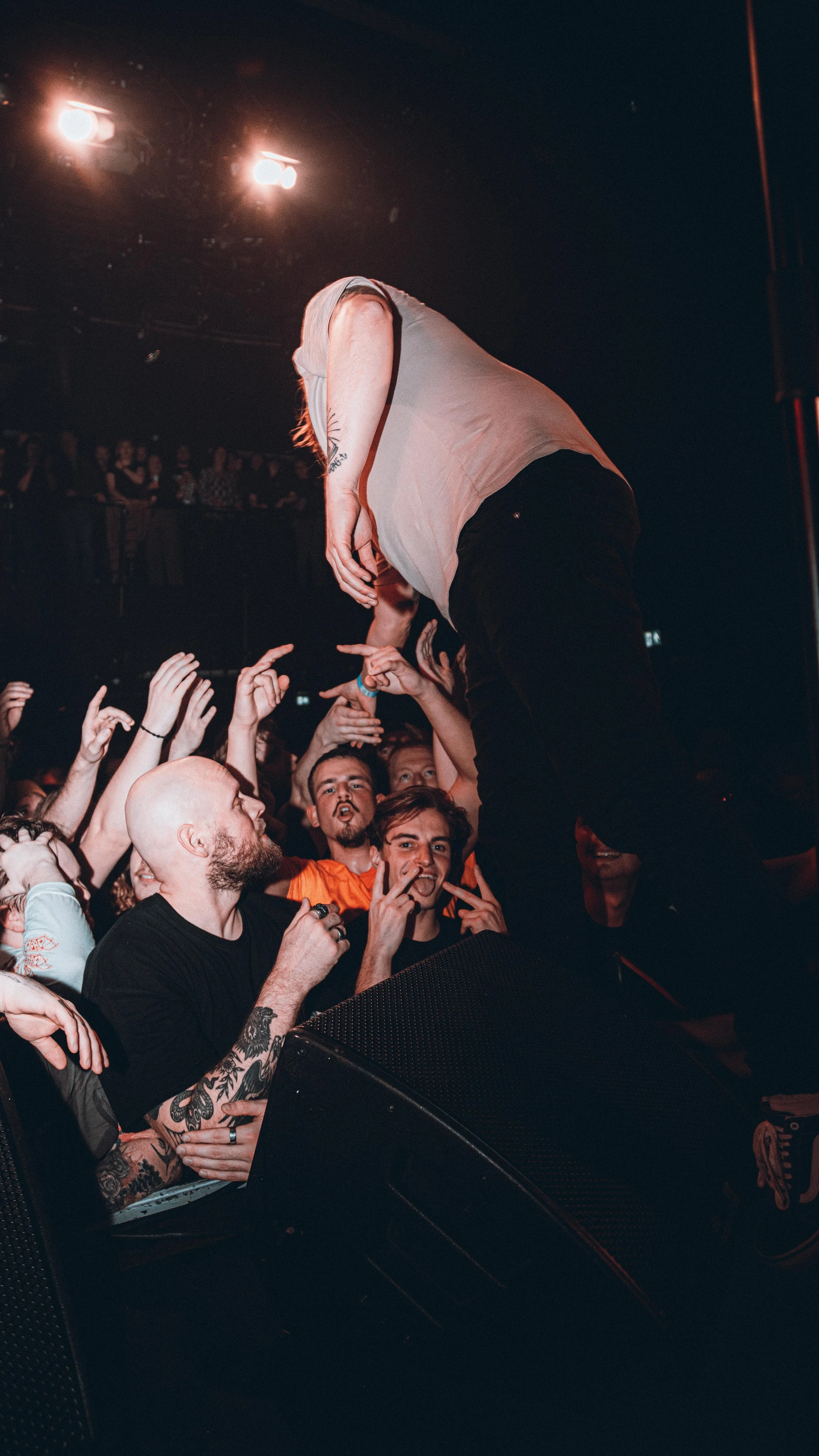 Musician crowd surfing at concert, crowd reaching up to touch them, stage lights overhead
